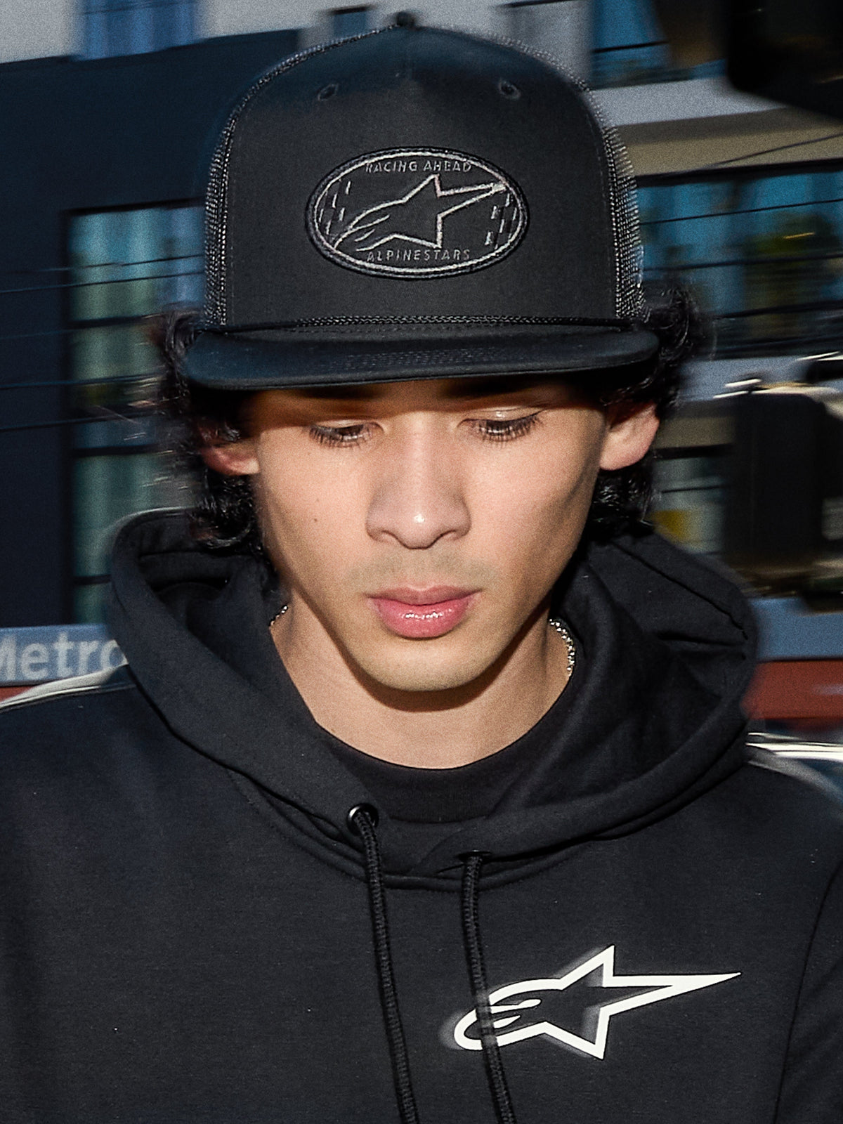 Boné Trucker Alpinestars Contender, boné casual preto com malha de poliéster na parte traseira, copa estruturada com remendo bordado do logótipo Astars, usado por um homem com hoodie preto Alpinestars, streetwear casual inspirado no desporto motorizado.