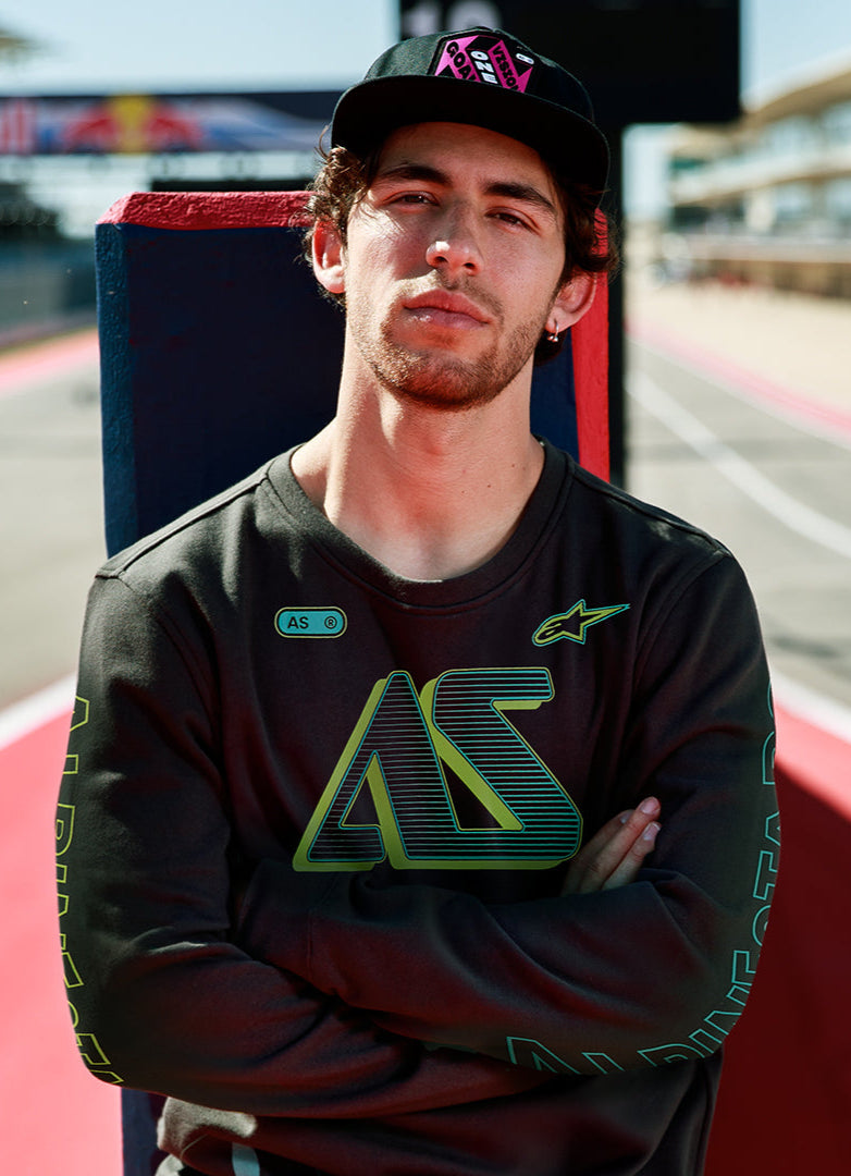 Alpinestars Ayess Csf Tee, t-shirt de manga comprida, preta, com grafismos AS em degradê verde e amarelo no peito e nas mangas, streetwear casual inspirado no desporto motorizado usada num circuito