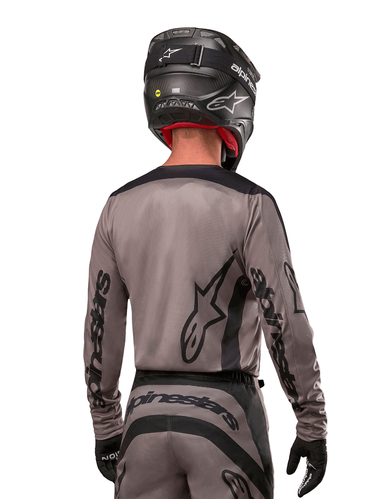 Piloto de motocross visto de costas a usar a camisola Alpinestars 2024 Fluid Lurv em Mud Black, com a marca Alpinestars em preto nas mangas e nas costas, acompanhado por um capacete preto e equipamento a condizer para corridas todo-o-terreno