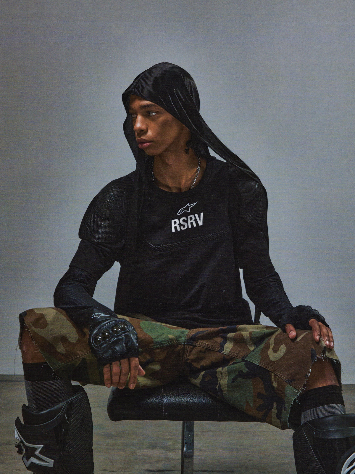 RSRV Nucleon SS Tee, Black T-shirt with white RSRV logo, worn with black hoodie, camouflage pants, fingerless gloves, and knee pads, urban tactical style, Alpinestars lifestyle collection