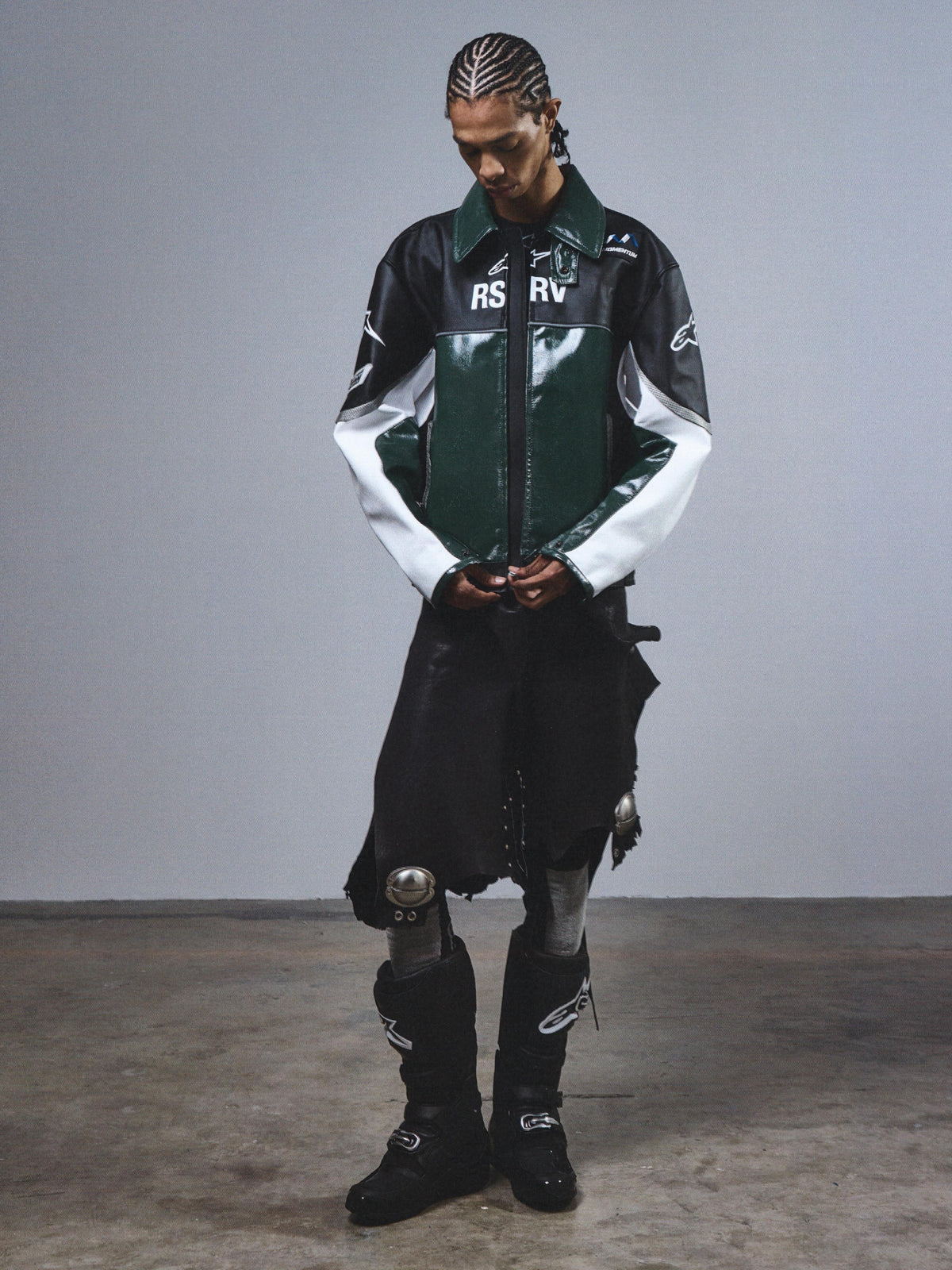 Alpinestars RSRV Alloy Leather Jacket, casaco de pele premium para motociclismo urbano, verde, preto e branco, acabamento brilhante, logótipos RSRV, fecho de correr frontal, design italiano de luxo, usado com botas pretas e calças pretas com detalhes metálicos