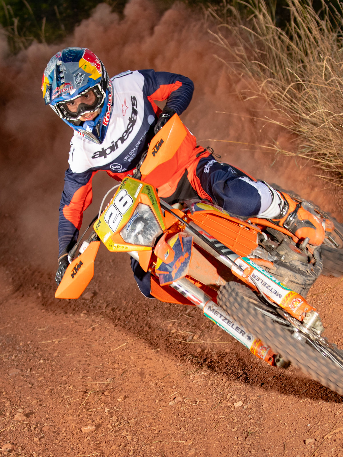 Piloto de enduro em ação numa moto de terra laranja, a usar a Camisola Alpinestars Pro-Dura em azul-marinho, laranja vibrante e branco, com um design leve e respirável e branding arrojado para performance off-road.