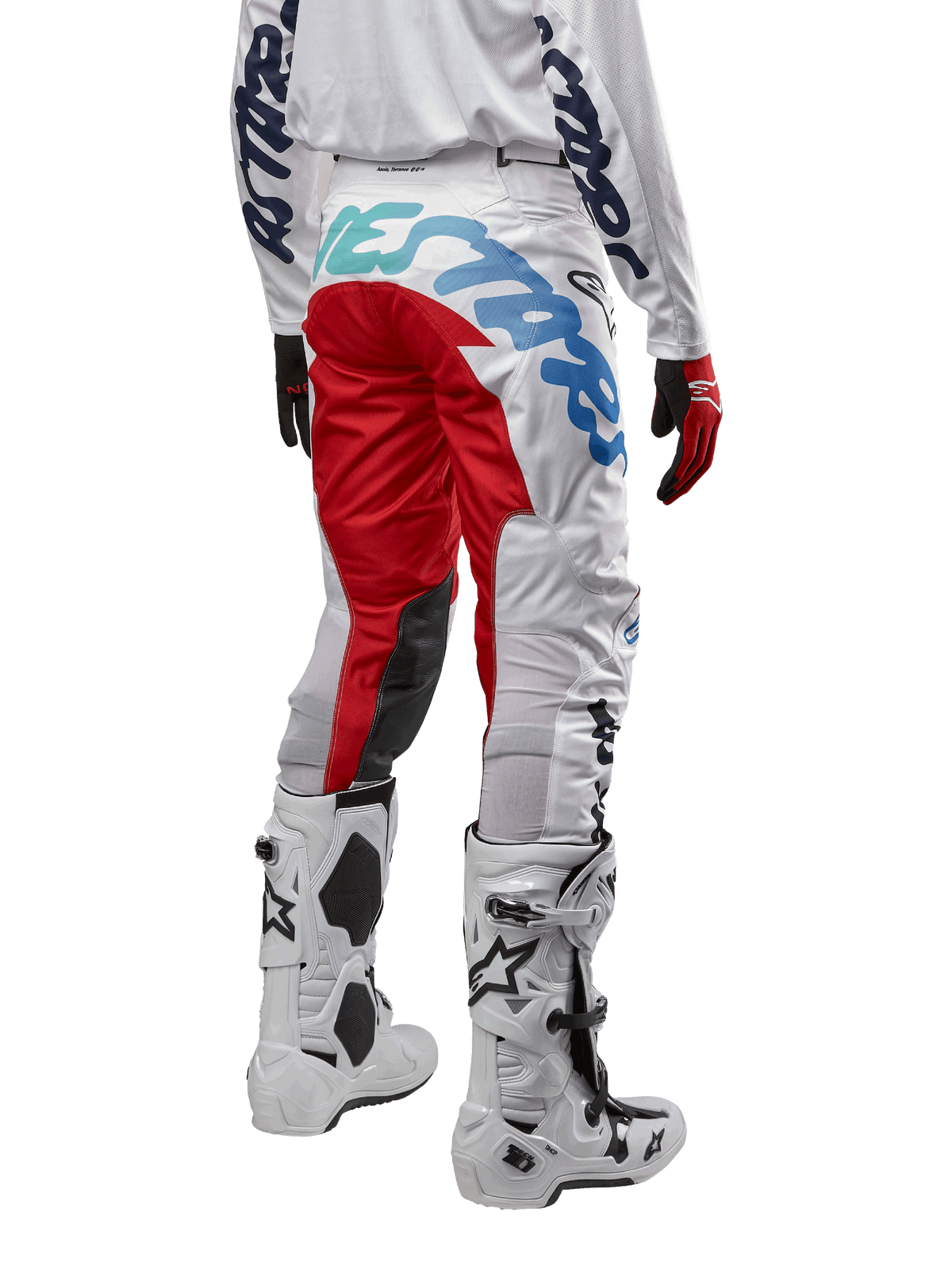 Alpinestars 2024 Racer Hana Pants, calças de motocross, brancas multicor com detalhes em vermelho e azul, vista traseira com logótipo grande no assento, usadas com botas de motocross brancas e pretas, concebidas para desempenho e durabilidade em todo-o-terreno