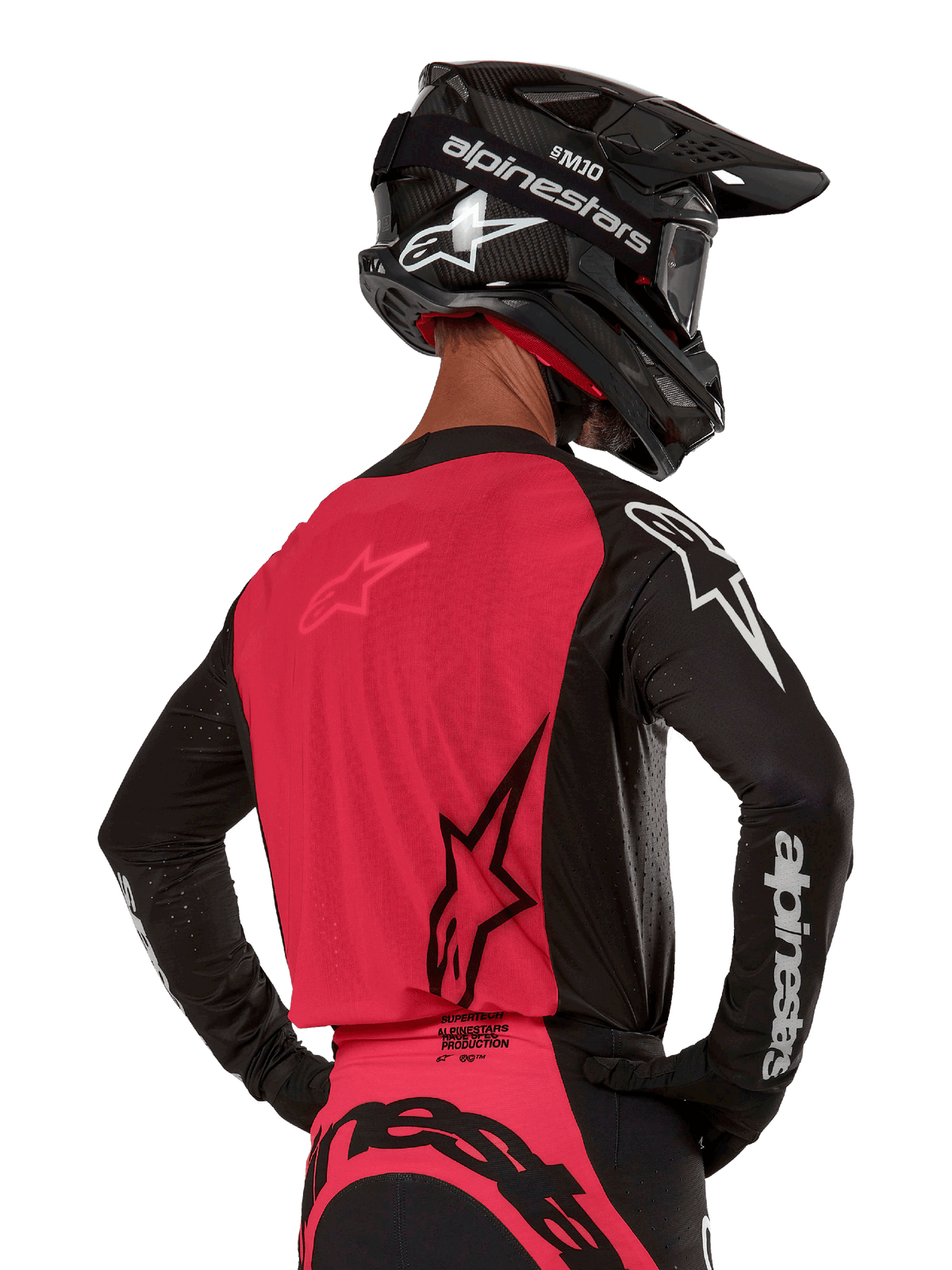 Alpinestars 2024 Supertech Ward Jersey, camisola de motocross, preto e vermelho berry, vista traseira com painel de malha vermelho e mangas pretas com logótipos brancos, usada com capacete de fibra de carbono preto e luvas, ajuste de corrida atlético para condução todo-o-terreno