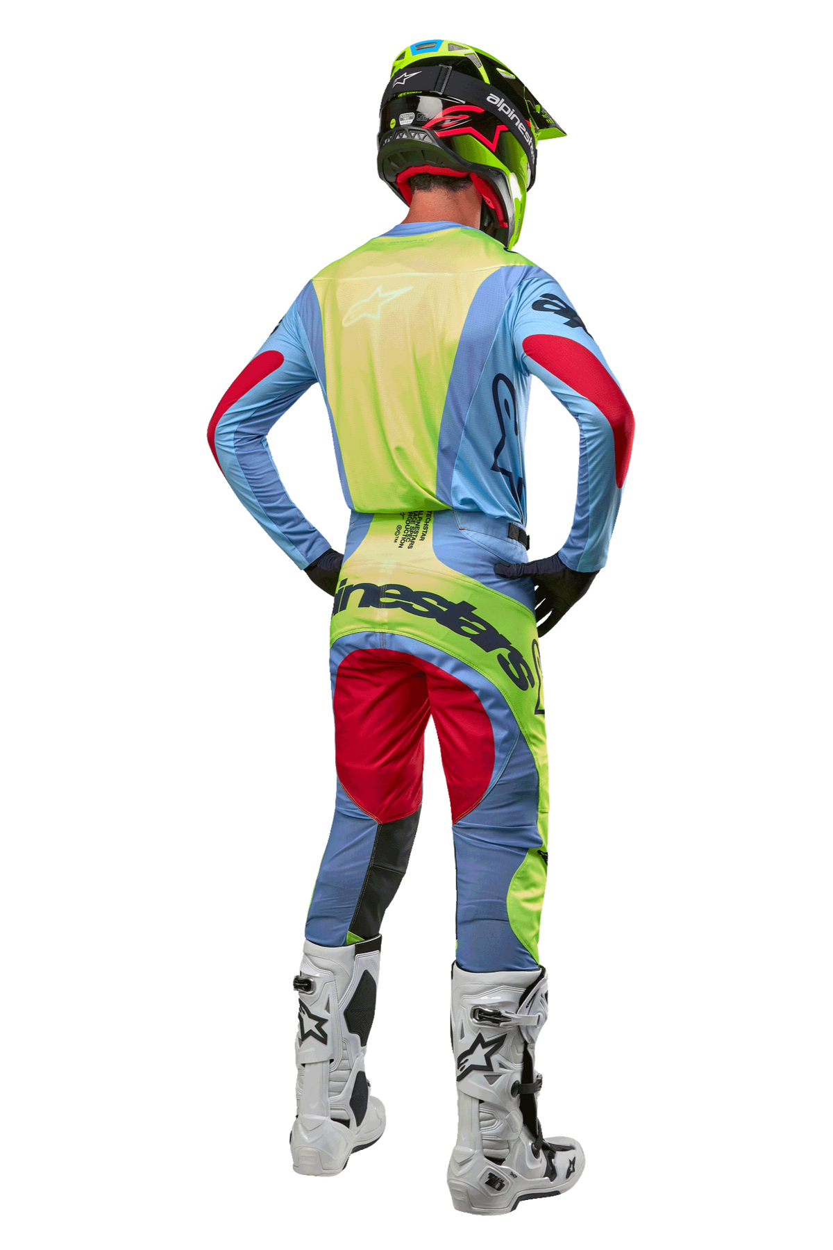 Piloto de motocross visto de costas a usar as calças Techstar Ocuri 2024 e a camisola a condizer, em azul claro, amarelo flúor e vermelho, botas brancas e pretas, capacete preto com detalhes néon, equipamento Alpinestars coordenado para corridas de todo-o-terreno