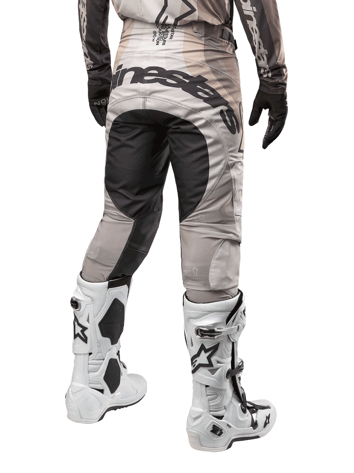 Alpinestars 2024 Techstar Pneuma Pants, calças de motocross, Areia Escura e Cinzento Poeira de Ferro, vista traseira da cintura para baixo, logótipo Alpinestars a preto no assento, usadas com botas de motocross brancas e pretas e luvas pretas, design durável de corte de corrida para competição todo-o-terreno