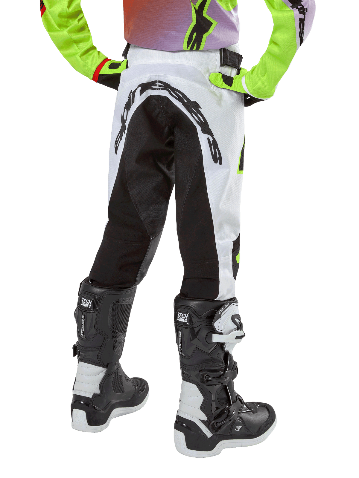 Alpinestars Youth 2024 Racer Lucent Pants, calças de motocross para jovens, brancas e pretas com detalhes néon, vista traseira mostrando o grande painel elástico traseiro e o logótipo Alpinestars, usadas com botas Alpinestars Tech Series pretas e brancas.
