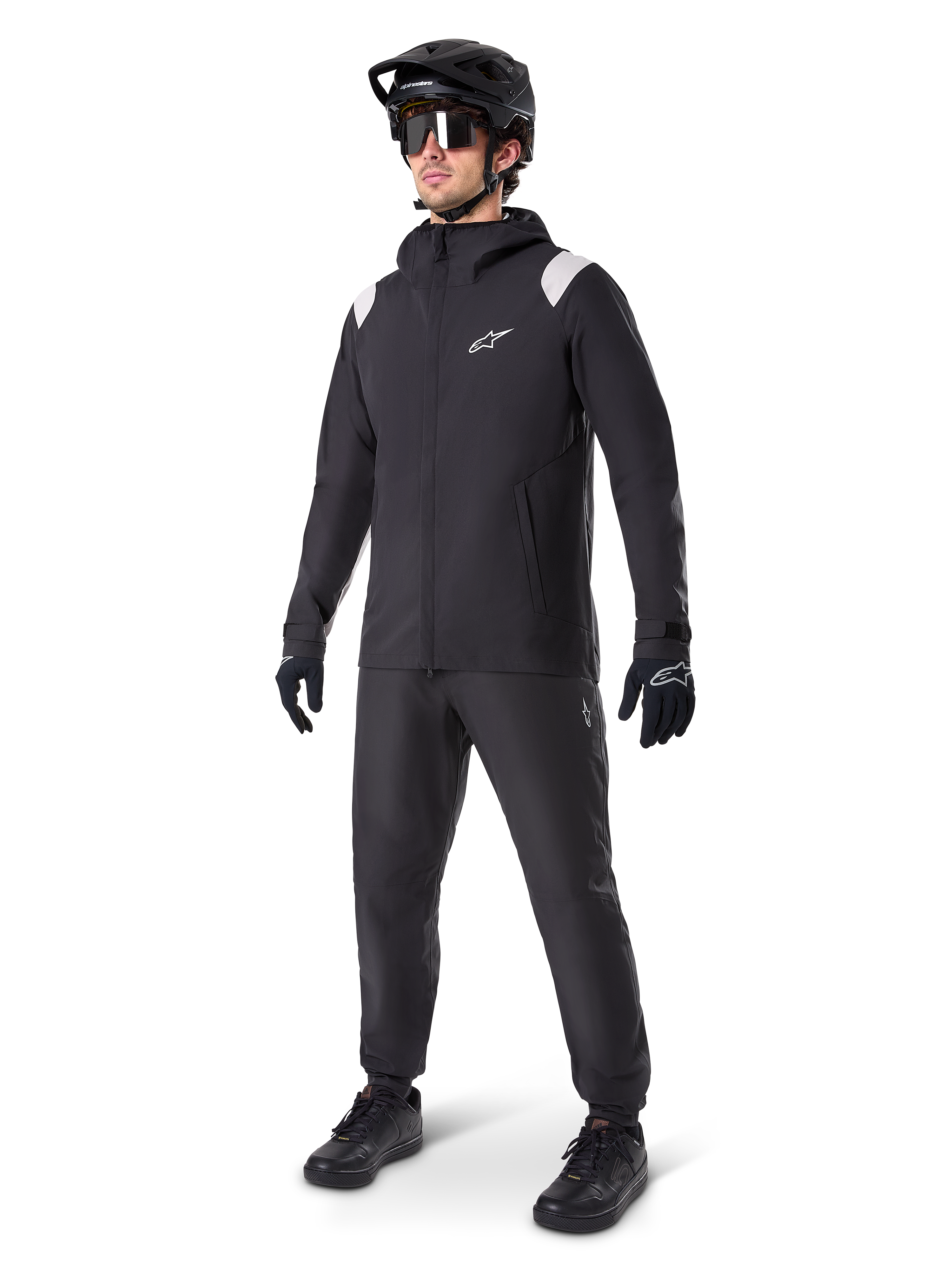Alpinestars A-Dura Rain Jacket, Black Mountain Bike Rain Jacket, featuring white shoulder accents, worn by a rider with matching black MTB helmet, sunglasses, gloves, and pants, technical all-weather cycling outfit