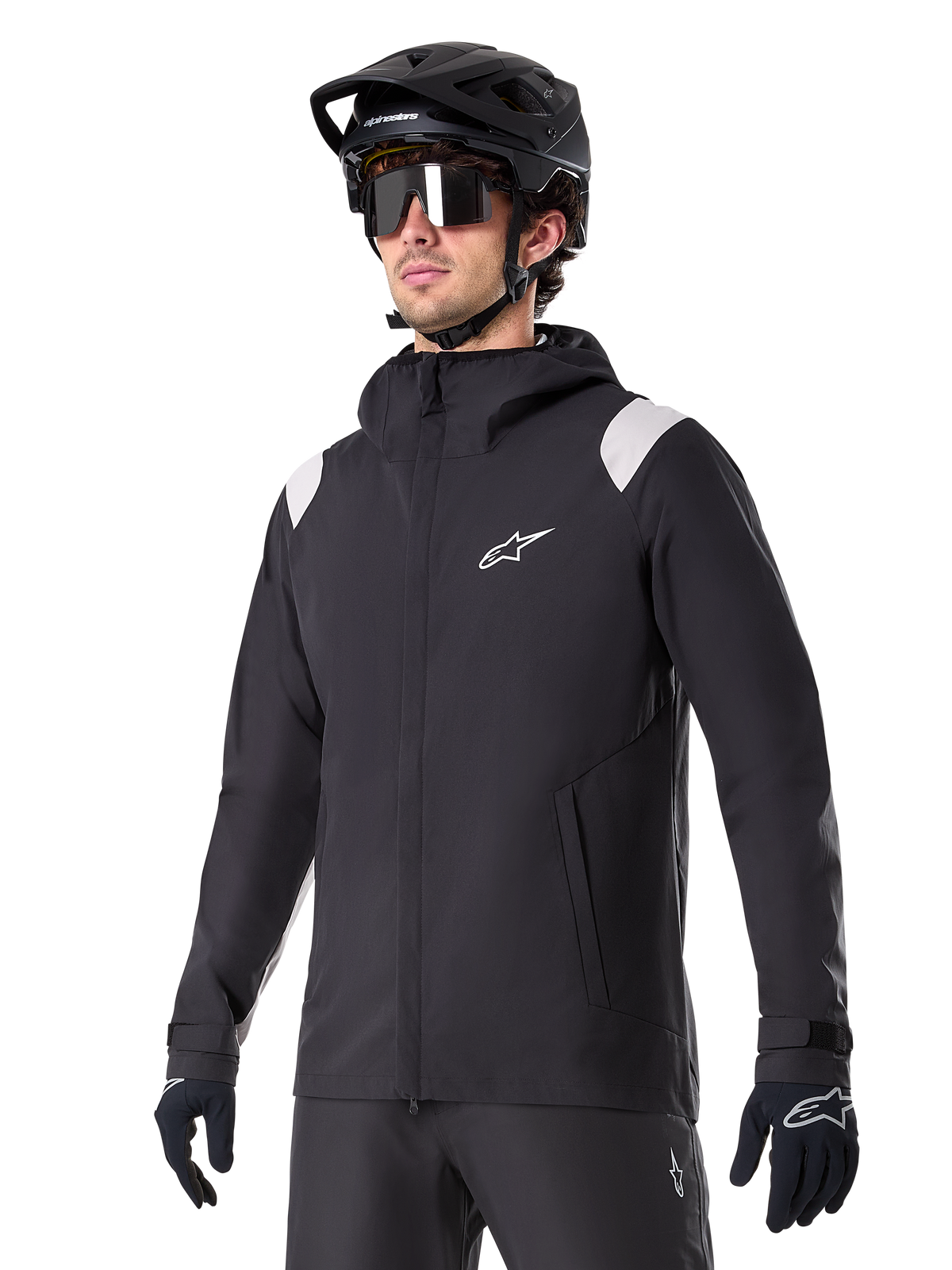 Alpinestars A-Dura Rain Jacket, casaco de chuva para mountain bike, preto com detalhes em cinzento claro nos ombros, usado por um ciclista com capacete de BTT preto e óculos de sol, logótipo branco no peito, construção impermeável, coordenado com calças e luvas pretas para ciclismo todo-o-terreno