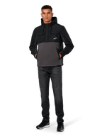 Alpinestars Juncture Hybrid Jacket, Black and Gunmetal, mixed-material anorak hoodie featuring a canvas fleece body and ripstop overlays, white A-star logo on chest, drawstring hood, worn by model with dark jeans and black sneakers, casual motorsport-inspired streetwear