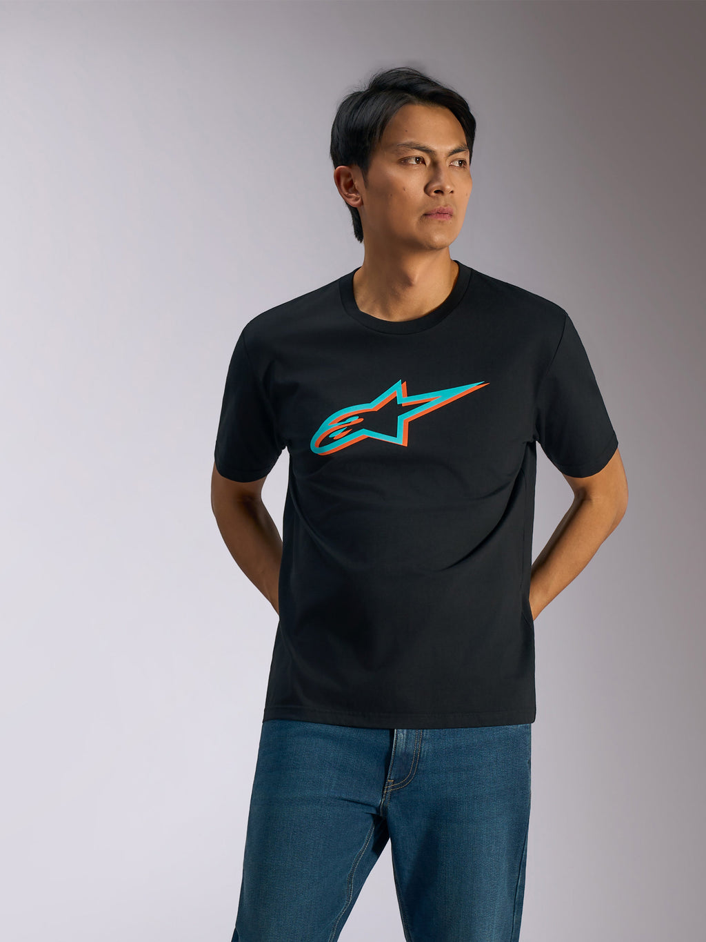 Alpinestars Ageless Shadow CSF Tee, t-shirt de manga curta, preta com logótipo em sombra turquesa e laranja, vestida por um homem com calças de ganga azuis, streetwear casual de estilo motorsport