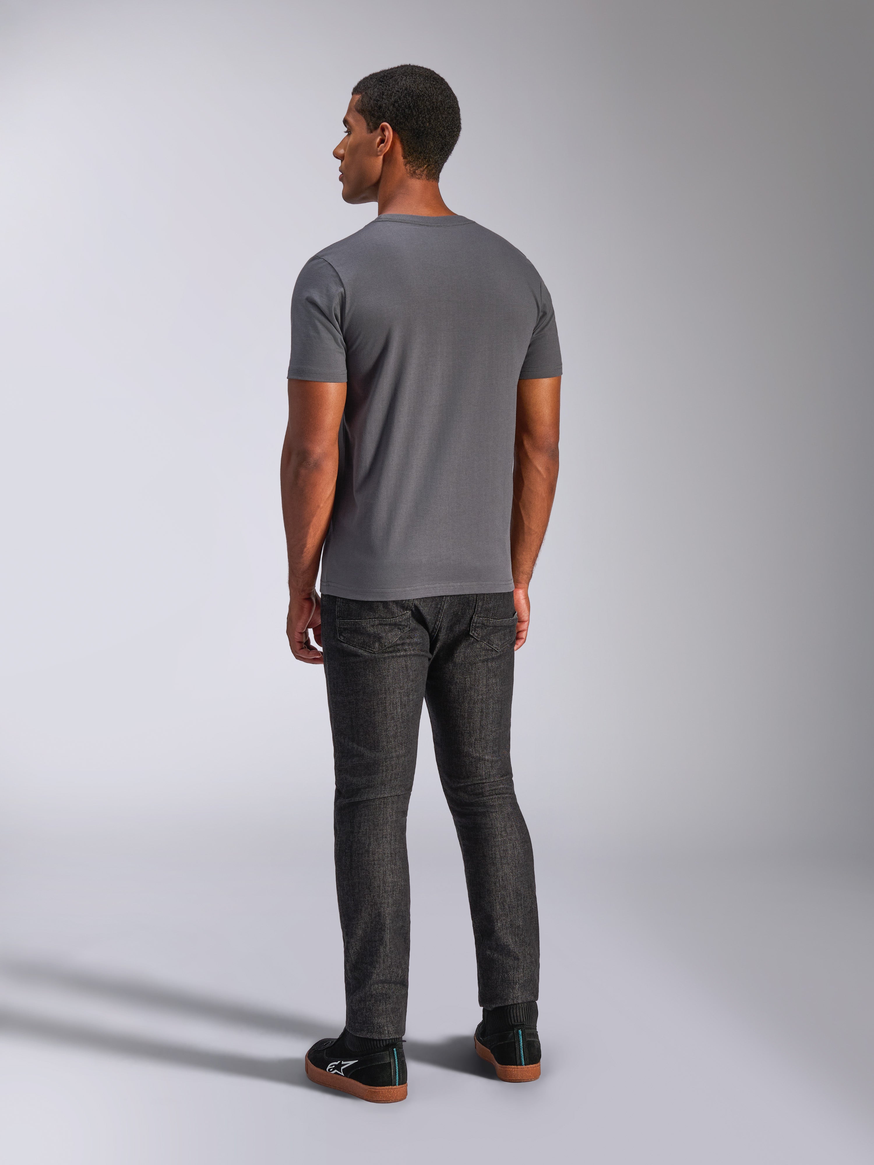 Alpinestars Always 2.0 CSF Tee, t-shirt de manga curta, cinzento antracite, vista traseira no modelo, combinada com calças de ganga escuras e sapatilhas pretas, streetwear casual inspirado no desporto motorizado