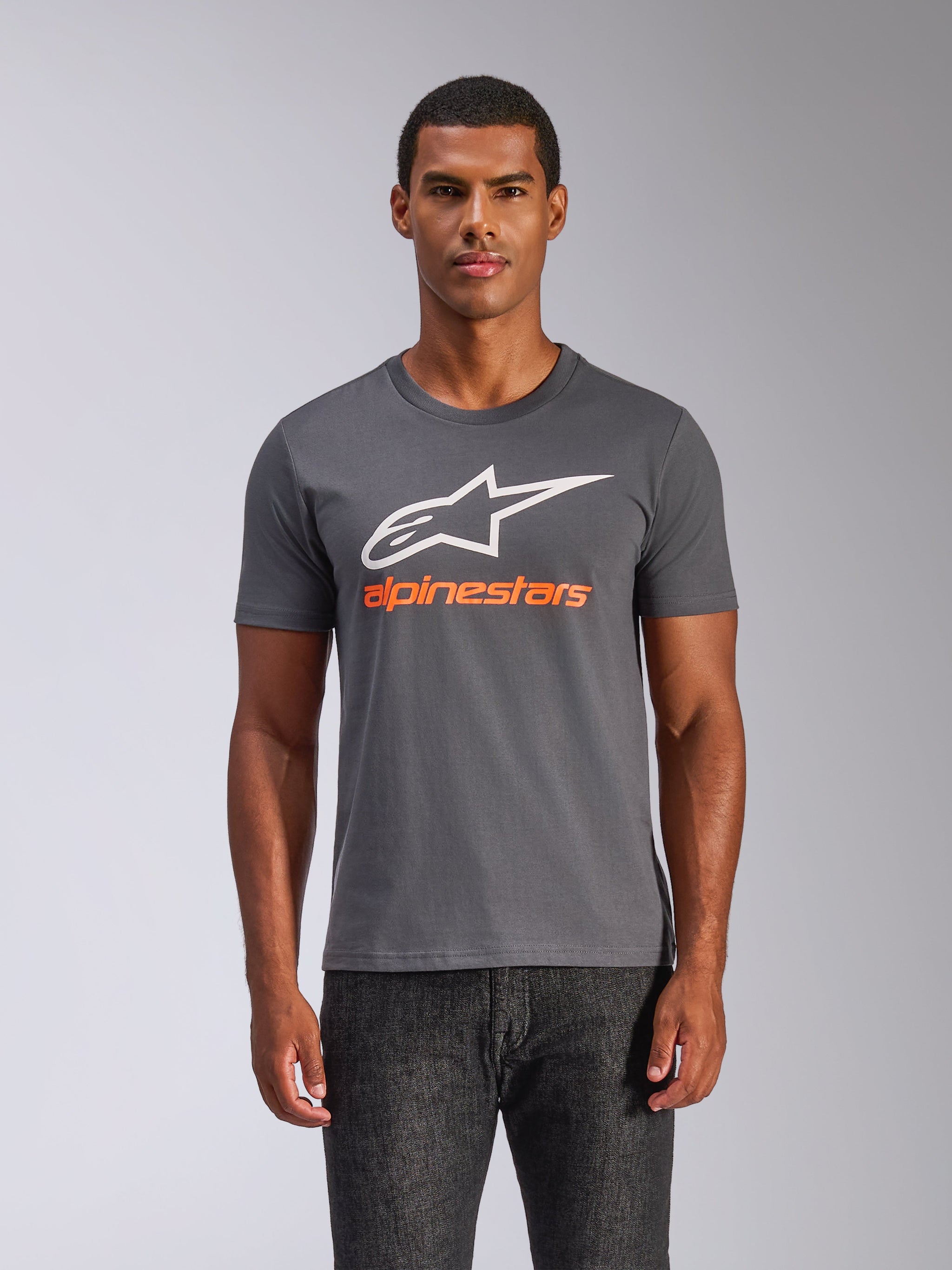 T-shirt Alpinestars Always 2.0 CSF, t-shirt de manga curta, cinzento carvão, logótipo A-star grande em branco com a marca Alpinestars em cor-de-laranja, vestida por um homem, roupa casual de estilo motorsport