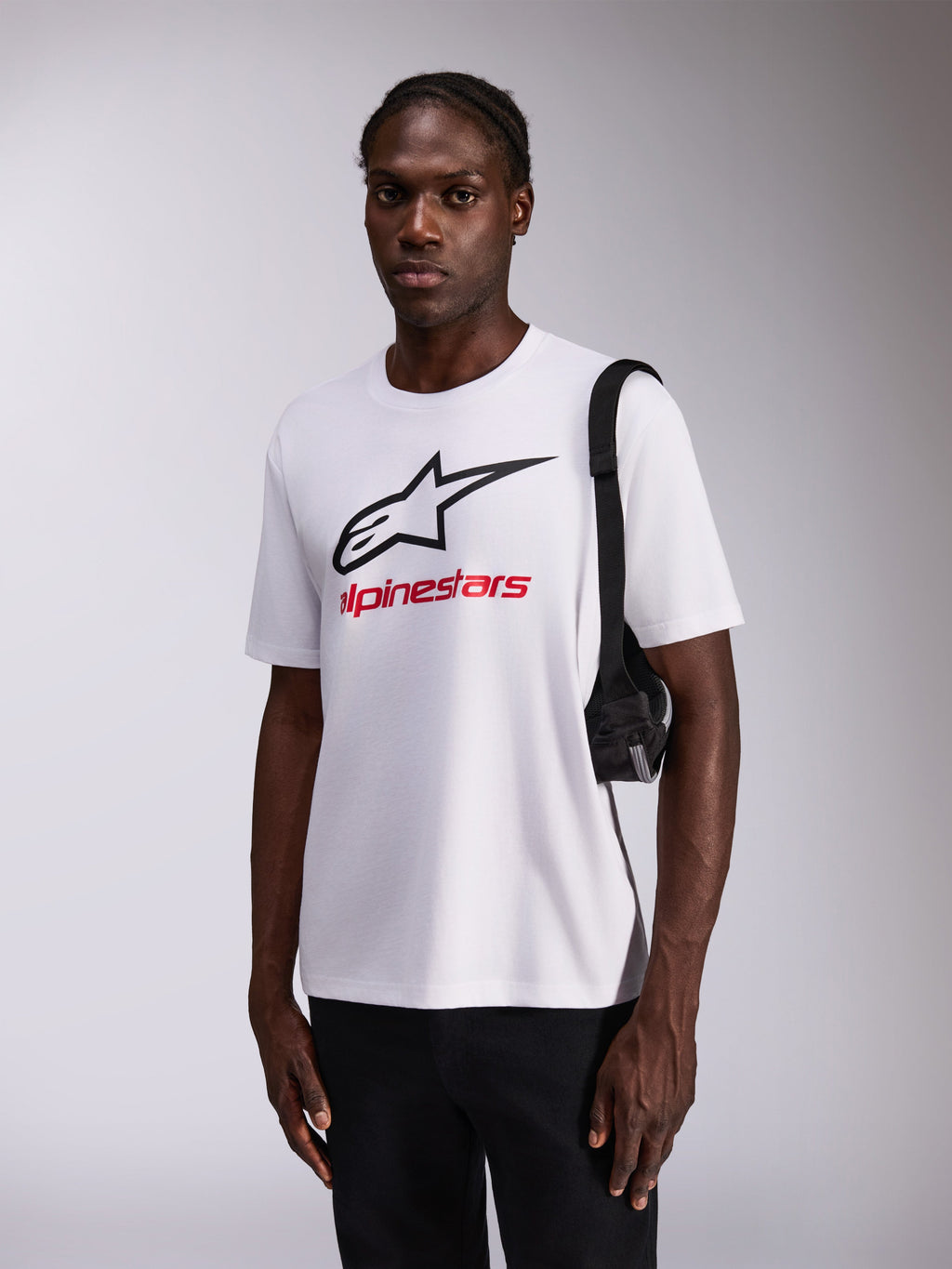 Alpinestars Always 2.0 CSF Tee, T-shirt de manga curta, branca com logótipo de estrela preto grande e marca a vermelho, usada por modelo com calças pretas e mala de ombro, streetwear casual inspirado no desporto motorizado