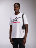 Alpinestars Always 2.0 CSF Tee, T-shirt de manga curta, branca com logótipo de estrela preto grande e marca a vermelho, usada por modelo com calças pretas e mala de ombro, streetwear casual inspirado no desporto motorizado