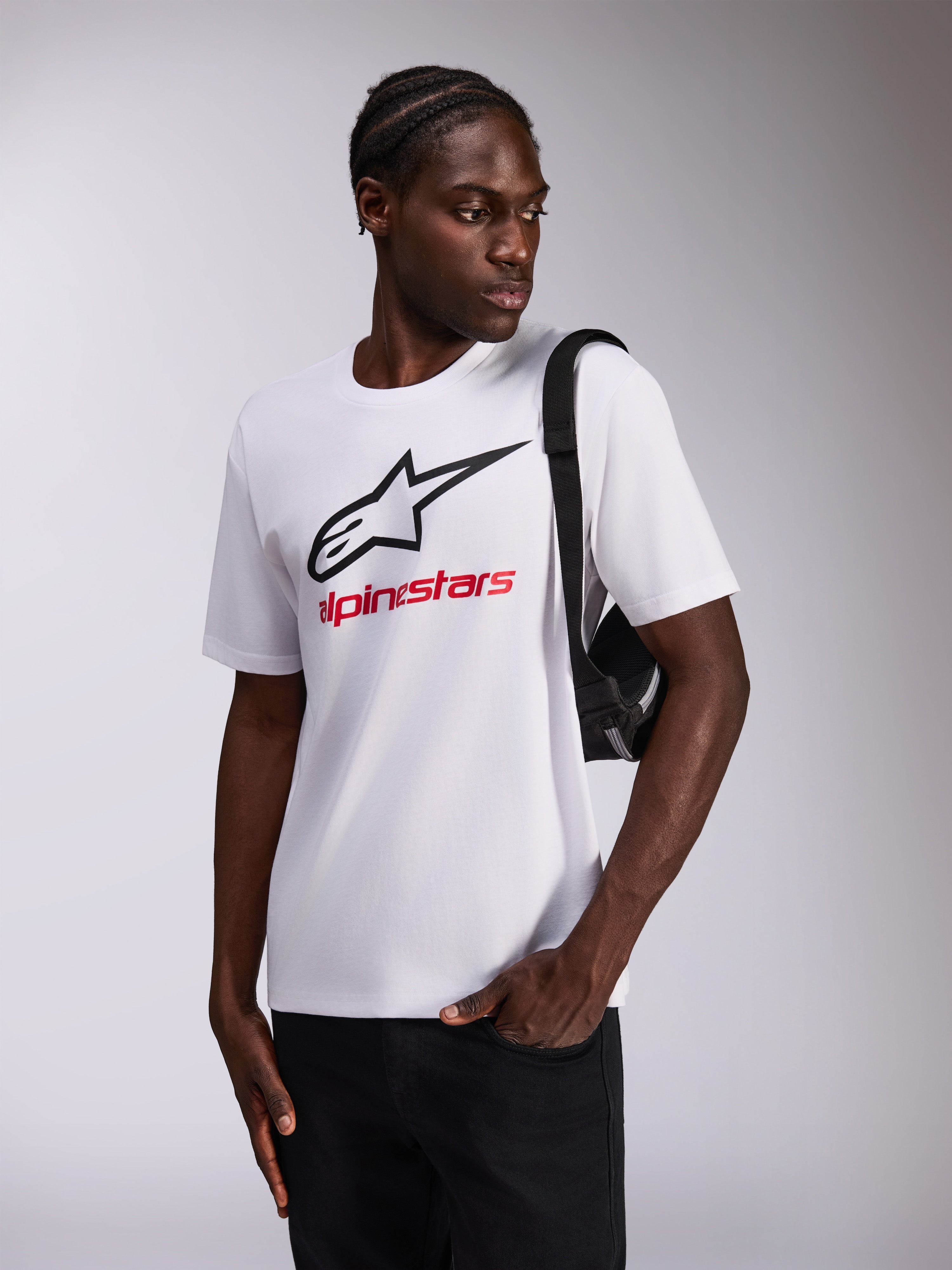 Alpinestars Always 2.0 CSF Tee, t-shirt de manga curta, branca, logótipo de estrela preto e texto Alpinestars vermelho, usada por modelo com mala a tiracolo preta, roupa desportiva casual de motorsport