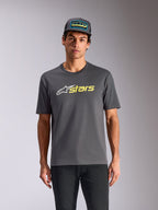 Alpinestars Blaze 2.0 CSF Tee, t-shirt de manga curta, cinzento carvão, logótipo de estrela branco e gráfico 'stars' em amarelo Hi-Vis, usada com boné trucker a condizer e calças pretas, streetwear casual de desportos motorizados