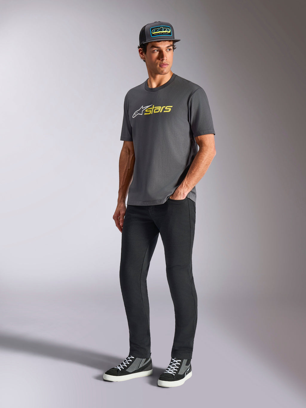 Alpinestars Blaze 2.0 CSF Tee, t-shirt de manga curta, cinza carvão com logótipo branco e amarelo de alta visibilidade, usada por um modelo com boné e calças pretas, vestuário casual de estilo de vida de desportos motorizados