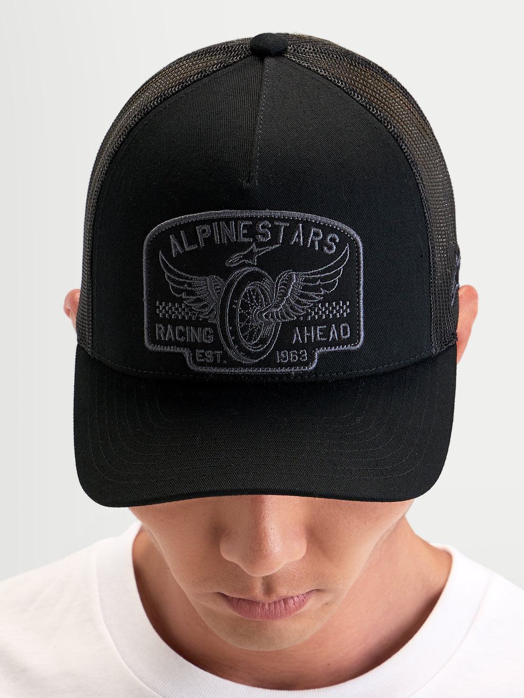 Alpinestars Boné Trucker Heritage Patch, boné desportivo casual preto e cinzento, aba curva, copa estruturada e malha de poliéster traseira, usado por uma pessoa