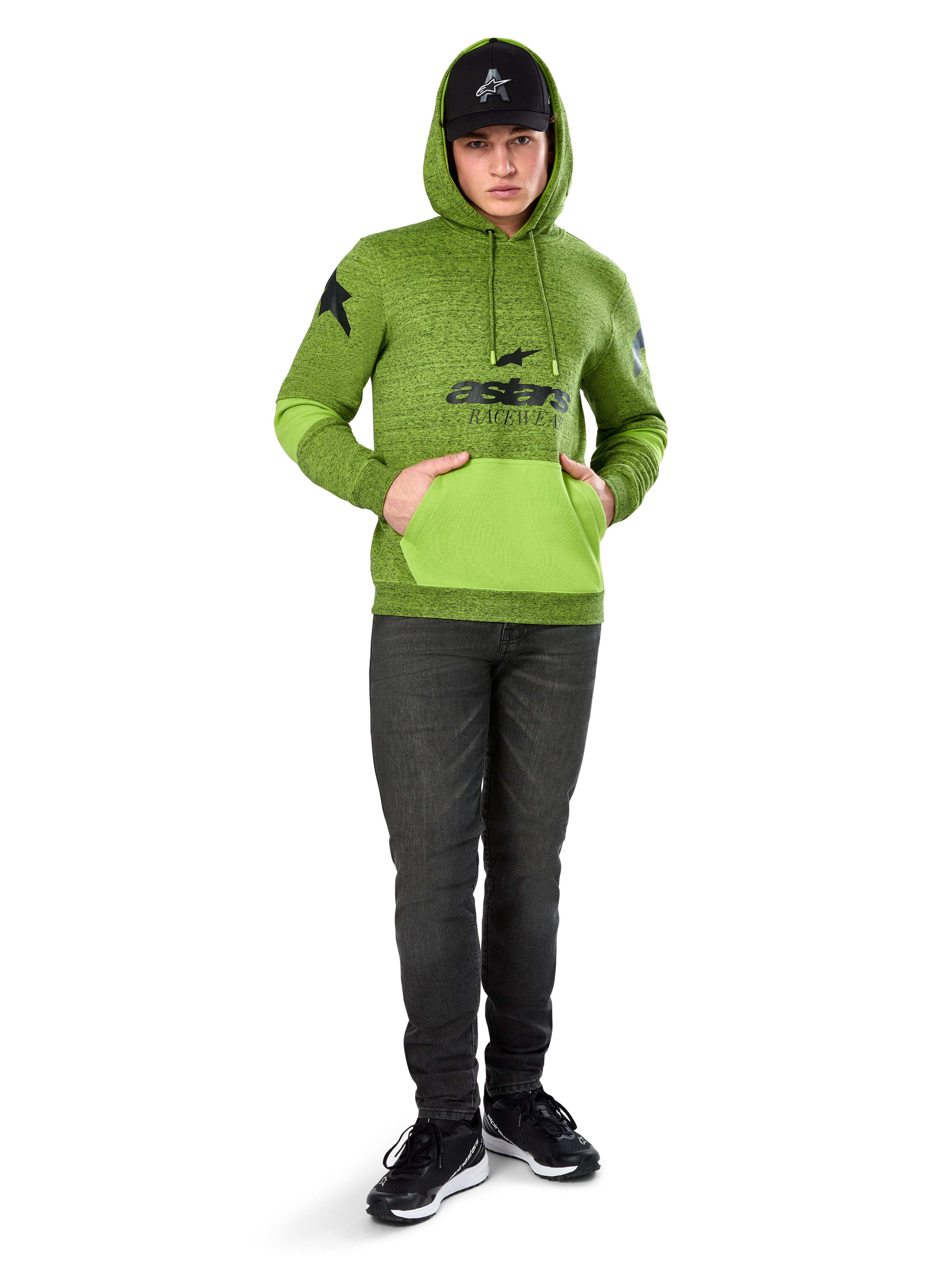 Alpinestars Hoodie Perpetuate, hoodie de lã em verde lima mesclado com bolso canguru e painéis nas mangas em verde vivo contrastante, grafismo frontal 'astars' a preto, combinado com um boné preto e calças de ganga escuras, streetwear casual inspirado no desporto motorizado