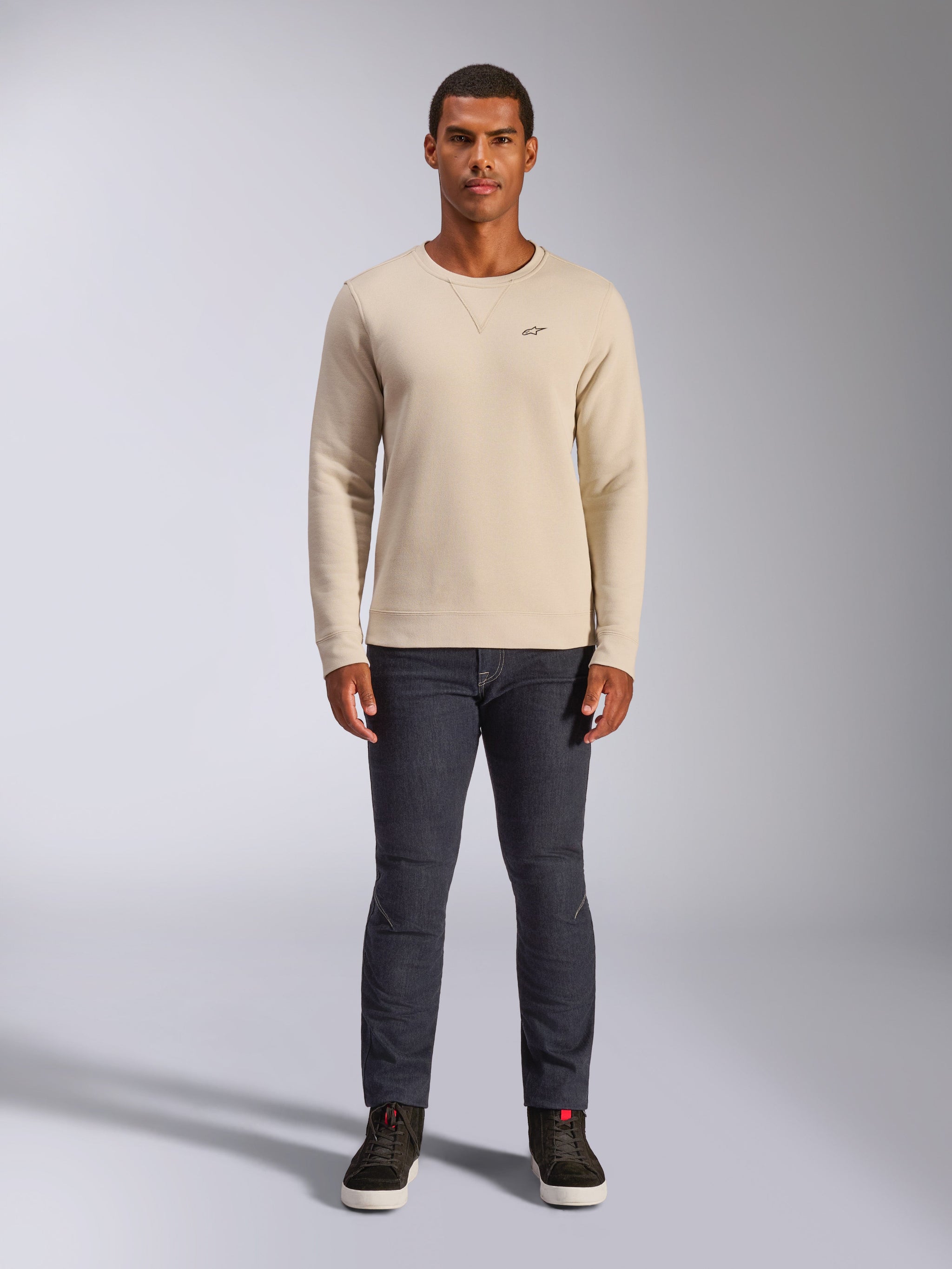 Alpinestars Positive Crew, camisola de gola redonda off-white, pequeno logótipo preto no peito, punhos e bainha canelados, costura triangular na gola, estilo casual motorsport streetwear usada com calças de ganga escuras