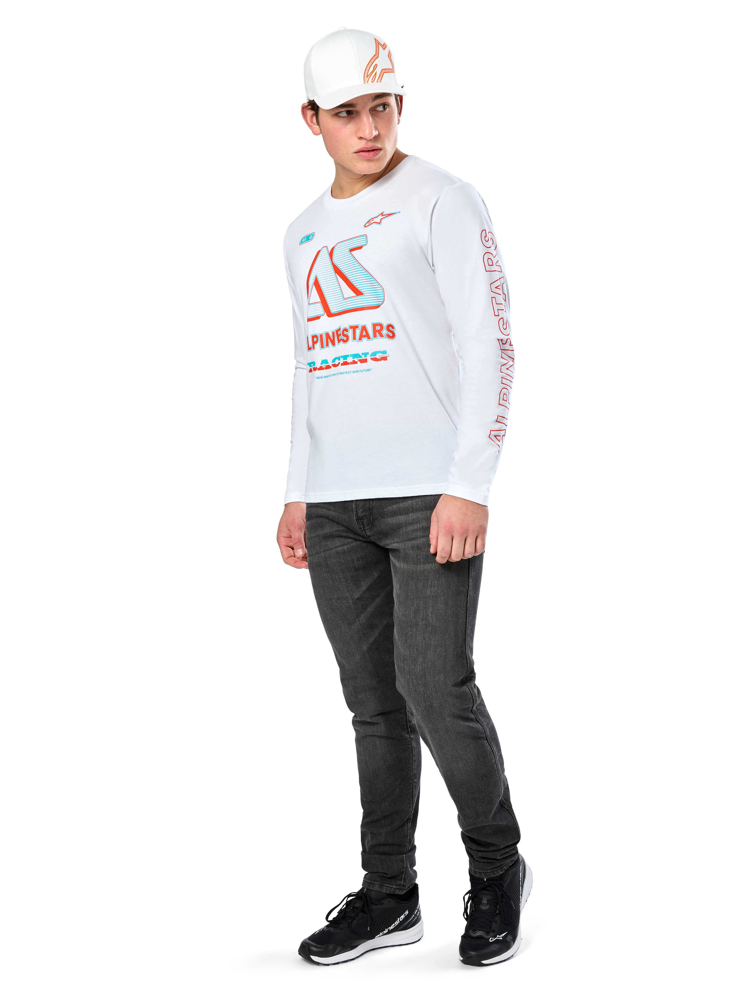 Alpinestars Ayess CSF Tee, T-shirt de manga comprida branca, com grandes grafismos de corrida CSF em azul e vermelho no peito e logótipo Alpinestars vermelho na manga, usada com calças de ganga escuras e um boné Alpinestars branco, streetwear casual de desportos motorizados