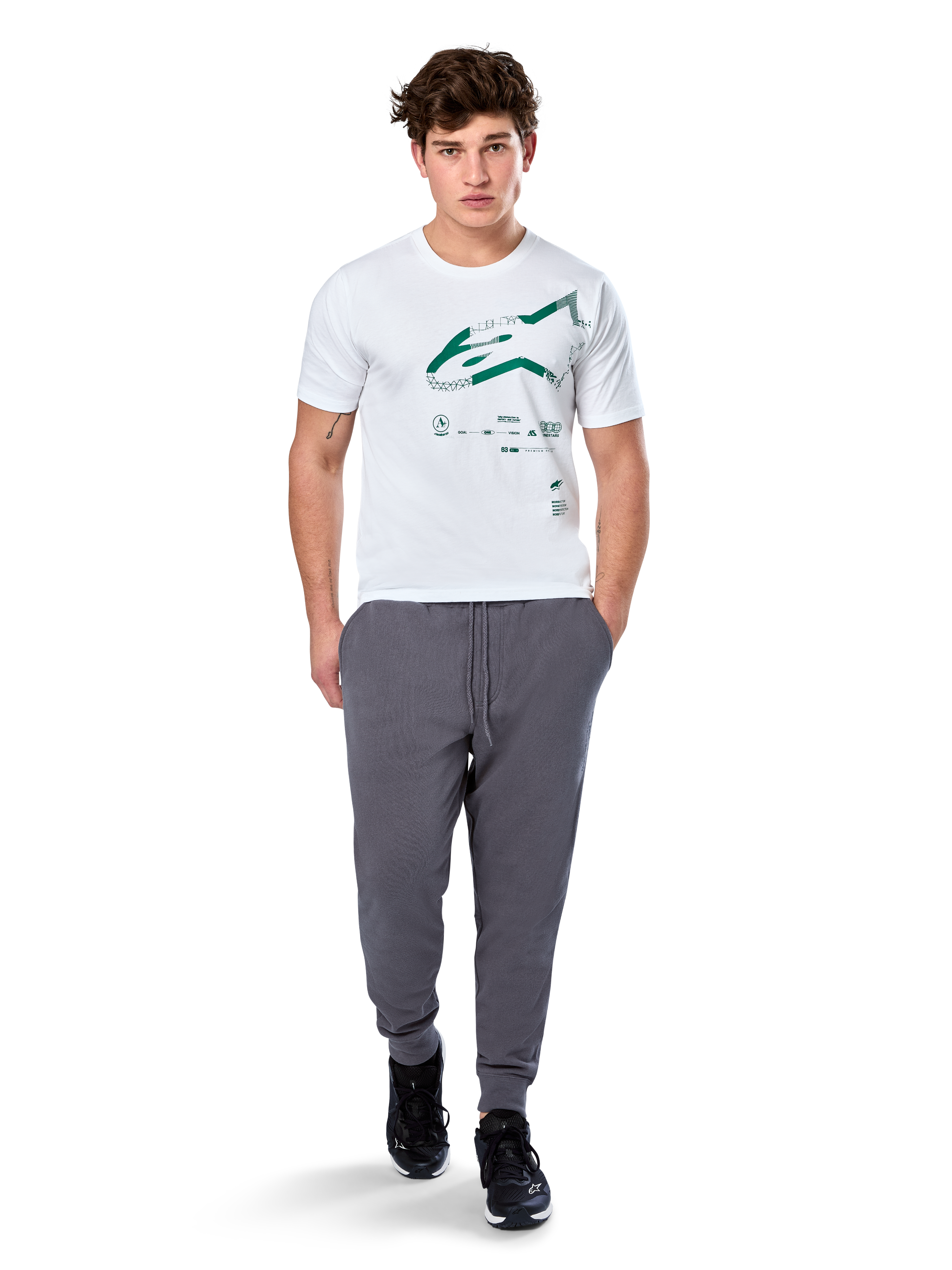 Alpinestars Geografica CSF Tee, t-shirt de manga curta, branca, logótipo Astars verde com gráfico geográfico multi-tech, acompanhada por calças de fato de treino cinzentas e sapatilhas pretas, streetwear casual de desportos motorizados