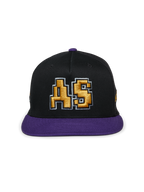 Alpinestars Franchise Hat, boné de pala plana preto e roxo, copa estruturada com pala e botão superior roxos, com logótipo "AS" bordado em 3D a dourado na frente, streetwear casual inspirado no desporto motorizado