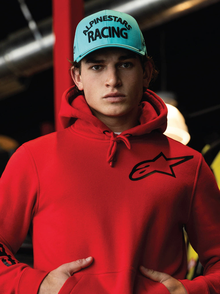 Boné Alpinestars Luminary, snapback de aba curva em azul aqua, bordado 3D preto com o texto 'ALPINESTARS RACING', usado com um hoodie Alpinestars vermelho vivo, estilo casual de desportos motorizados e streetwear