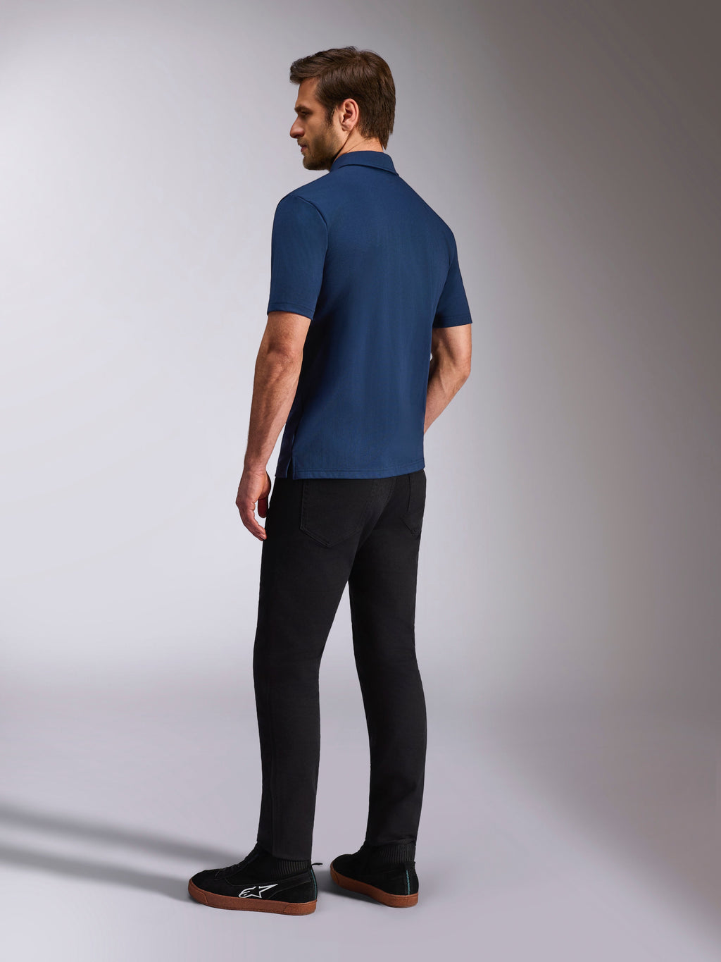 Polo Alpinestars Impetus Sport, polo de manga curta azul marinho, vista lateral e traseira no modelo, combinado com calças pretas e sapatilhas pretas, vestuário desportivo casual de estilo de vida motorsport