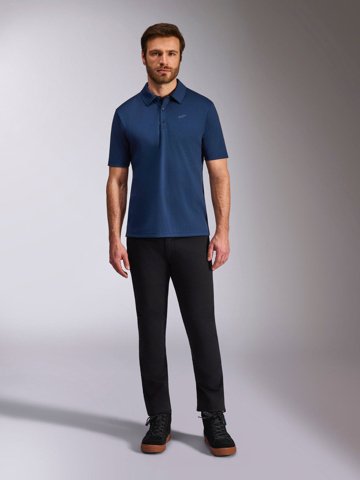 Alpinestars Impetus Sport Polo, polo de manga curta, azul-marinho, pequeno logótipo Astars prateado no peito, carcela de três botões, usado por modelo com calças e botas pretas, vestuário desportivo casual inspirado no desporto motorizado