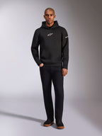 Alpinestars Insight Hoodie, black pullover hoodie with white Astars logo on the chest and sleeve, worn by a model with black pants and black sneakers, casual motorsport-inspired streetwear