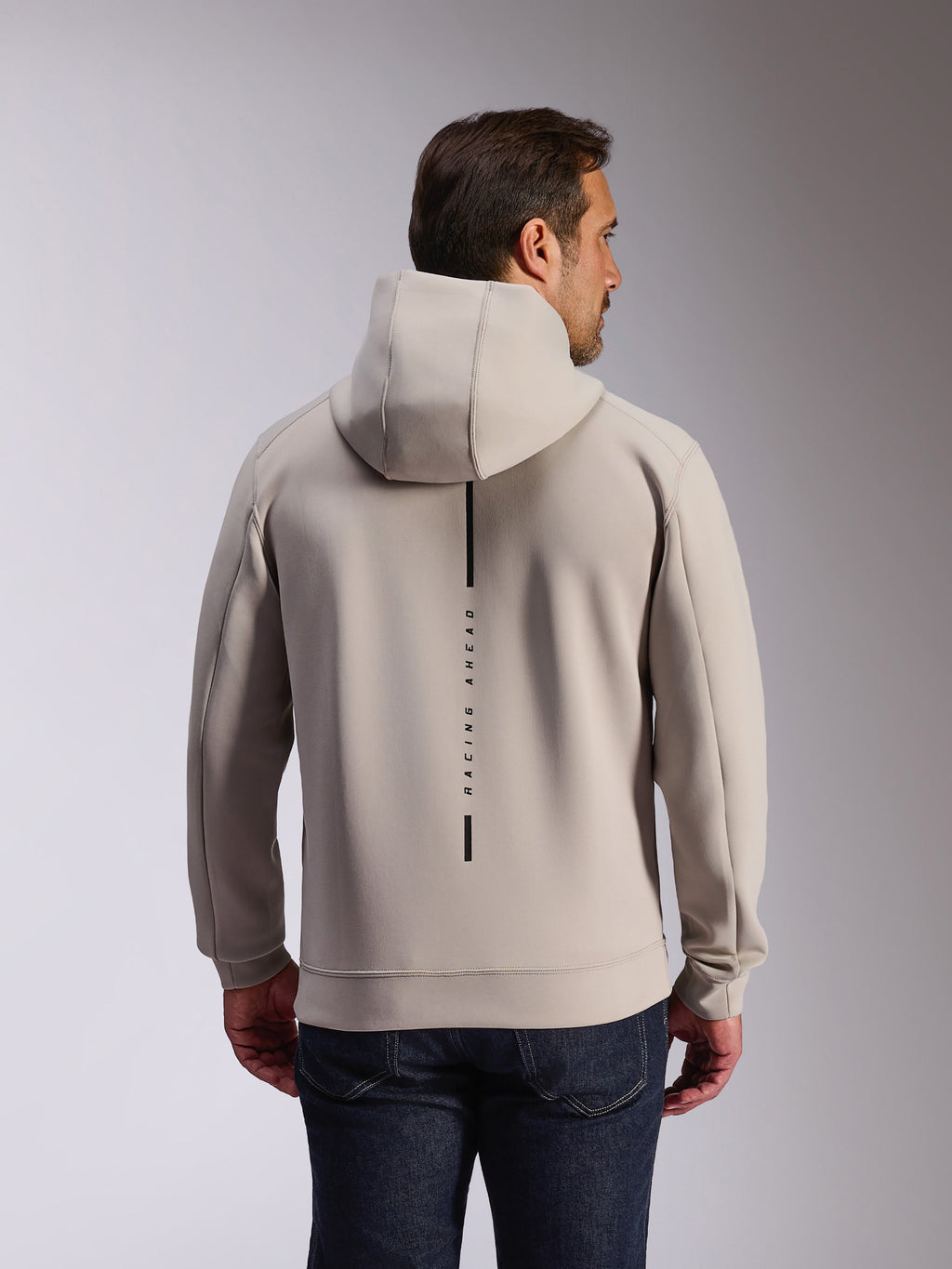 Alpinestars Insight Hoodie em Cement, vista traseira de modelo a usar uma sweatshirt cinzenta clara com capuz, apresenta um logótipo de risca vertical preta com o texto 'RACING AHEAD', hoodie casual de lã de dupla face inspirado no desporto motorizado.