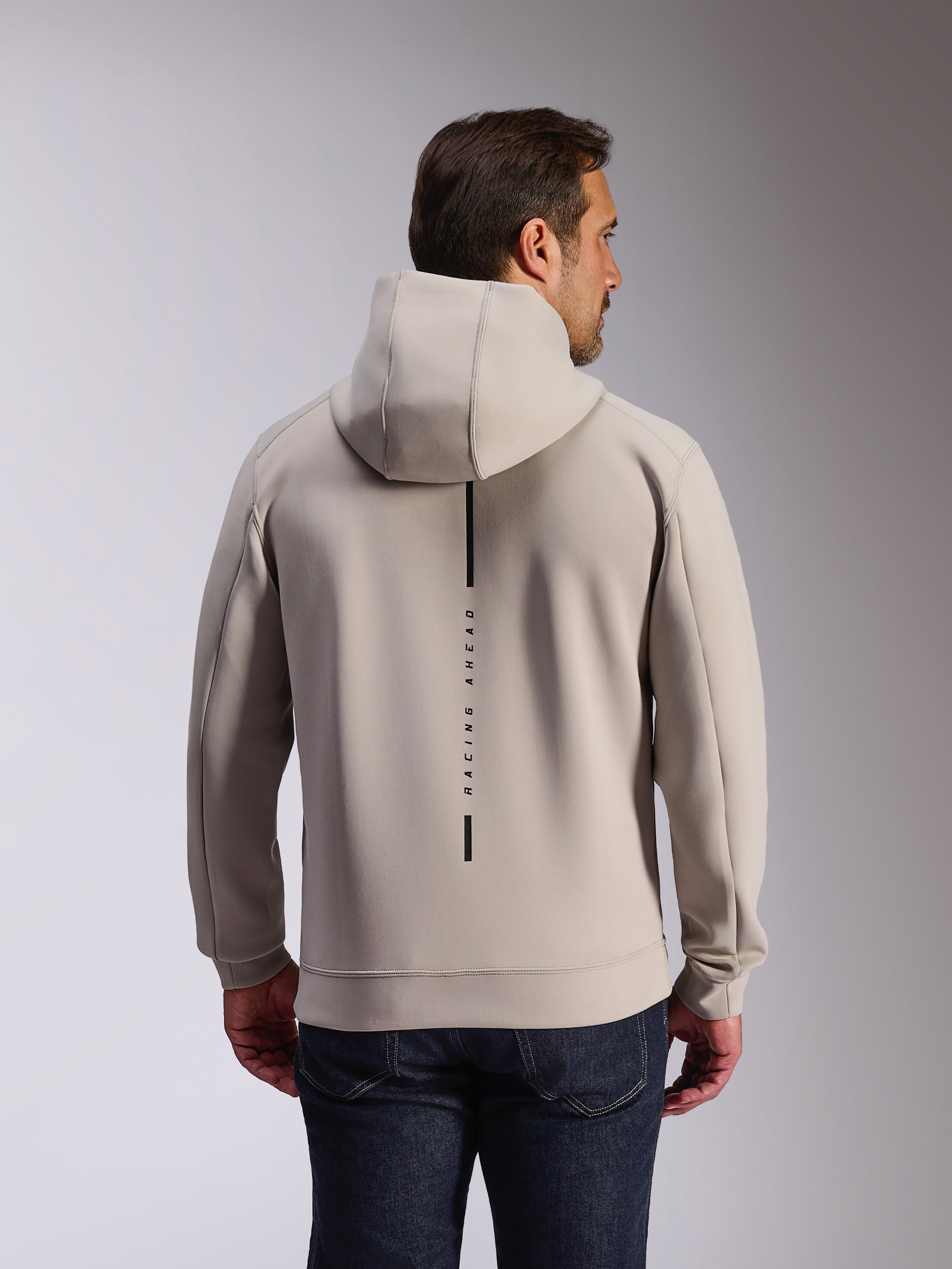 Alpinestars Insight Hoodie em Cement, vista traseira de modelo a usar uma sweatshirt cinzenta clara com capuz, apresenta um logótipo de risca vertical preta com o texto 'RACING AHEAD', hoodie casual de lã de dupla face inspirado no desporto motorizado.