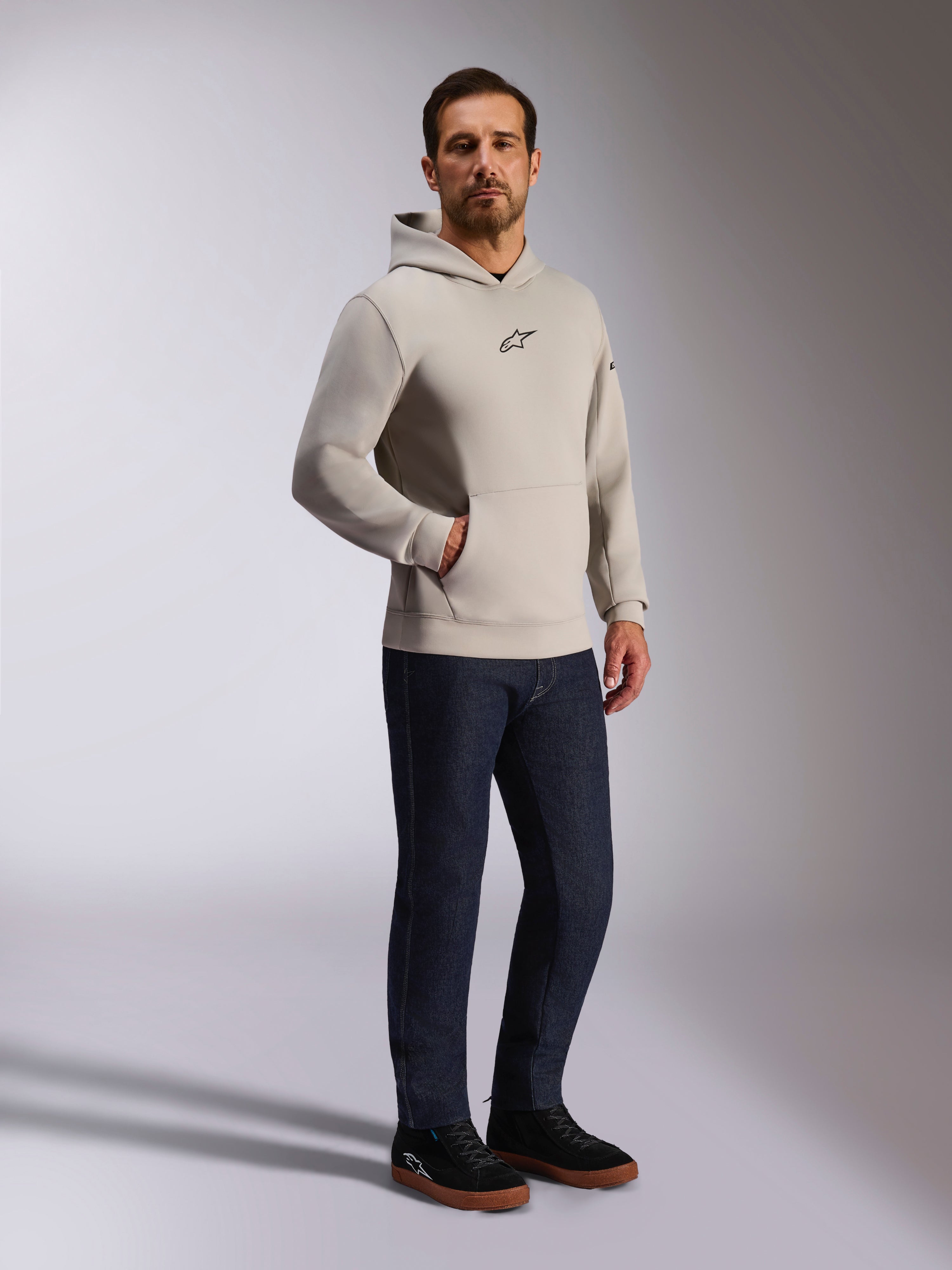 Alpinestars Insight Hoodie, casual streetwear, cinzento Cement com logótipo Astars preto no peito, design pullover com bolso canguru, usado com calças de ganga azul escuro e ténis pretos, estilo moderno inspirado no desporto motorizado