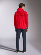 Alpinestars Emergent Oversized Hoodie, vermelho, vista traseira num modelo masculino, apresentando o logótipo Alpinestars bordado em 3D tom sobre tom, usado com calças de ganga azul escura, streetwear casual inspirado no desporto motorizado