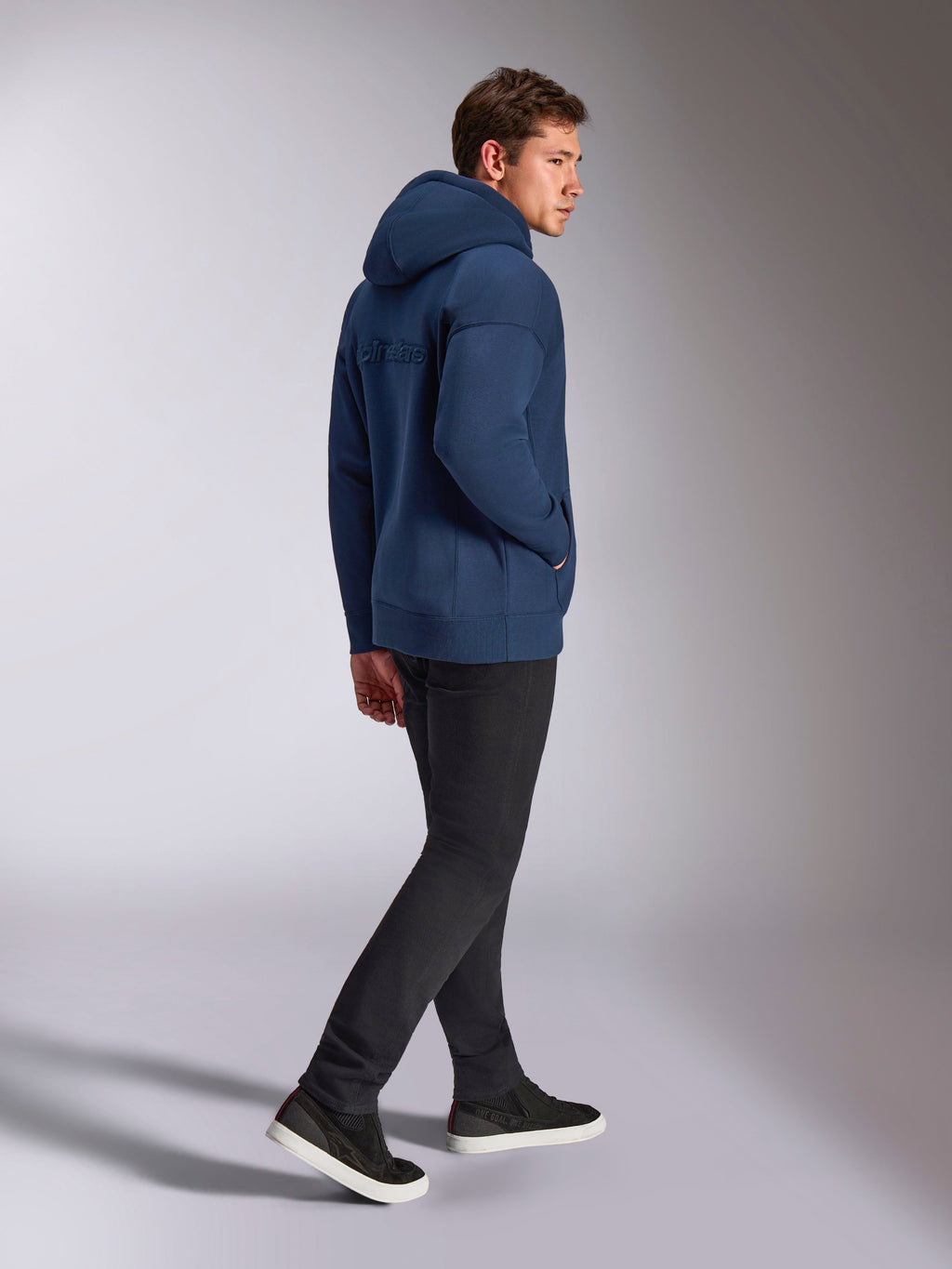 Alpinestars Emergent Oversized Hoodie in Navy Blue, back view showing 3D embroidered Alpinestars word logo, oversized fleece fit with drawstring hood, worn with black pants, casual motorsport-inspired streetwear