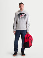 Alpinestars Camisola Com Capuz Obsessed, camisola de fleece para homem, cinzenta com gráficos inspirados em MX a vermelho e preto, logótipos nas mangas, modelo masculino a segurar mochila Alpinestars vermelha.