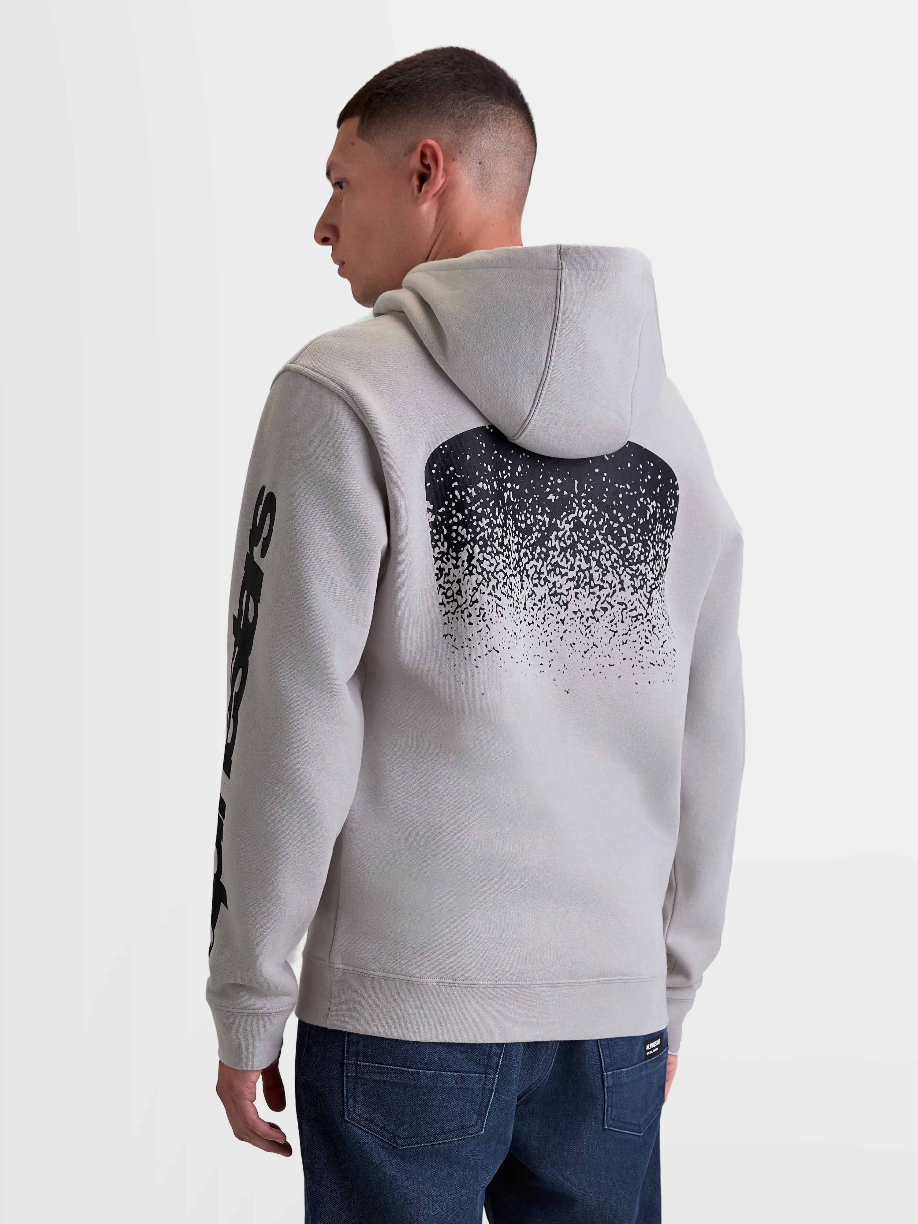 Alpinestars camisola com capuz Obsessed, camisola em fleece para homem em cinzento cimento, com grande gráfico traseiro preto em gradação inspirado em MX e marca na manga, vista traseira no modelo, vestuário casual motorsport.