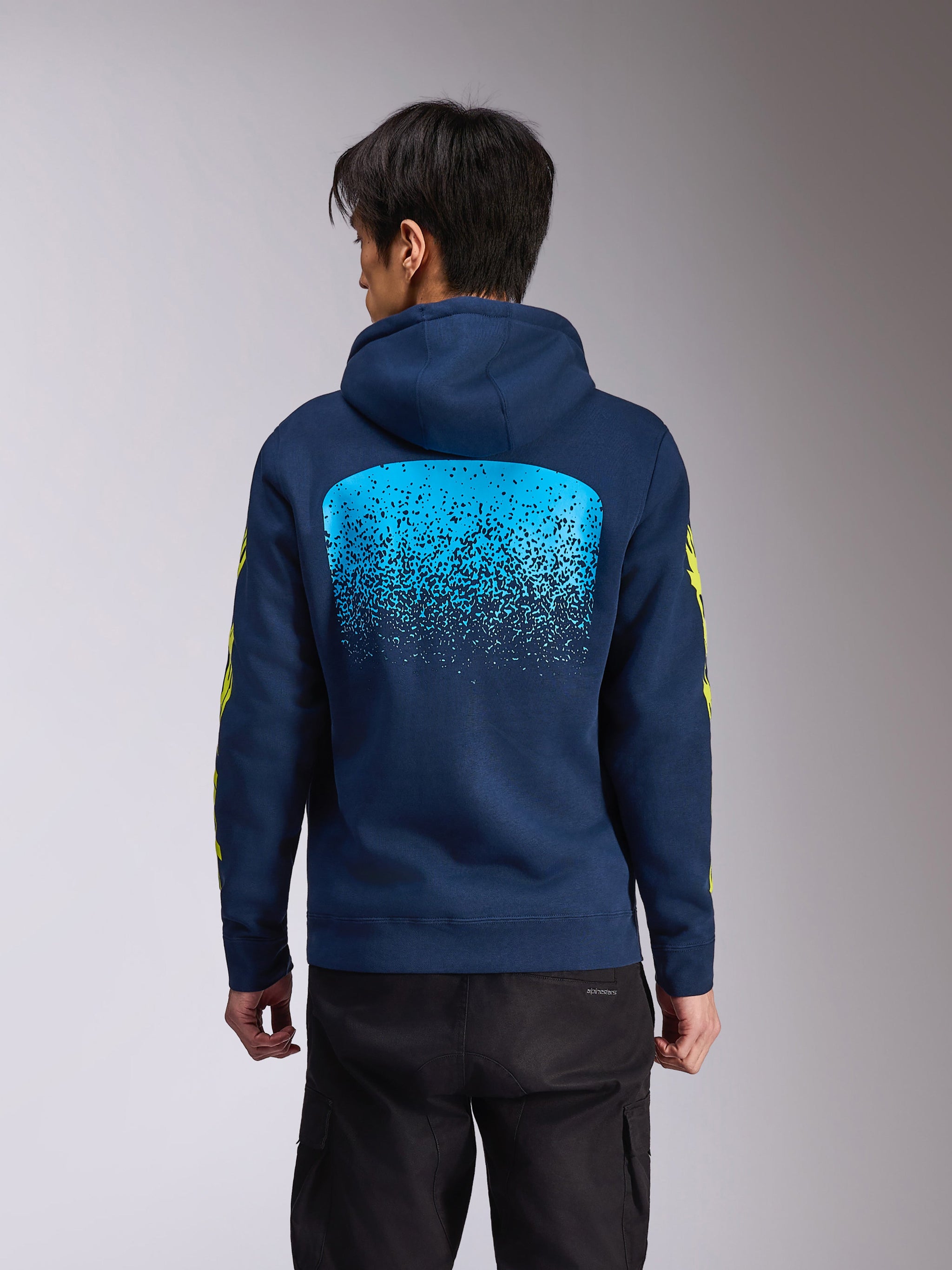 Alpinestars Obsessed Hoodie, camisola com capuz em fleece azul-marinho, vista traseira com um grande gráfico de gradação MX em azul claro, logótipo Alpinestars amarelo nas mangas, streetwear casual inspirado no desporto motorizado