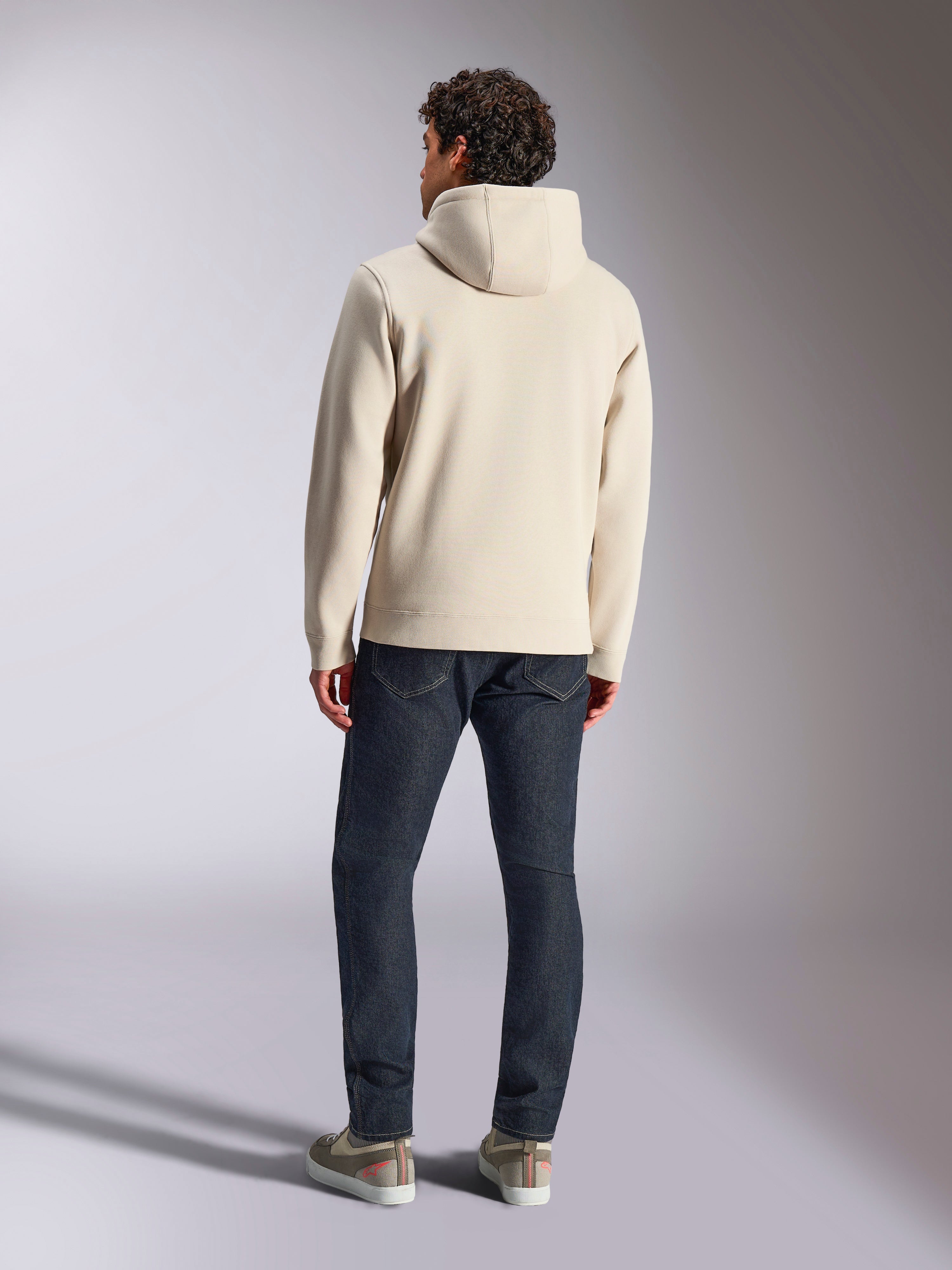 Alpinestars Pulse Hoodie, Off White, vista traseira de um homem a usar uma camisola com capuz de fleece casual com calças de ganga escuras e sapatilhas, design desportivo moderno
