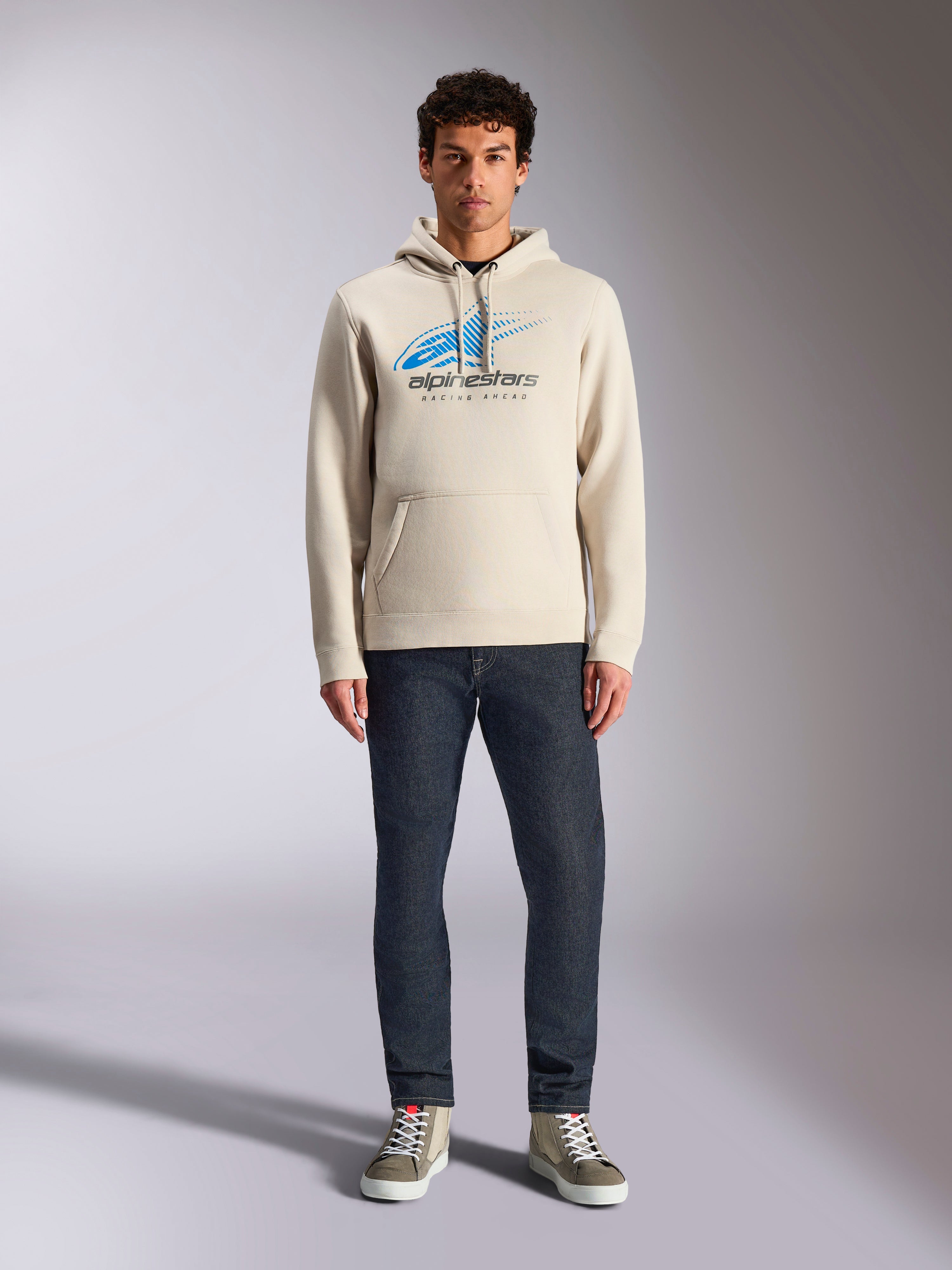 Alpinestars Pulse Hoodie, Off White, camisola de manga comprida com capuz e cordão, logótipo Astars Combo azul e preto com efeito de desvanecimento speed line, combinada com calças de ganga escuras e sapatilhas, streetwear casual de desportos motorizados