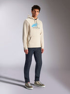Alpinestars Pulse Hoodie, streetwear casual em Off White, camisola com capuz em fleece com logótipo Astars azul e cinzento com efeito speed line, bolso canguru, usada por modelo com calças de ganga escuras e sapatilhas de cano alto.