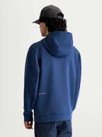 Alpinestars Camisola Com Capuz Cypher, hoodie de sportswear em azul aço, vista traseira num modelo mostrando o capuz de gola alta forrado em malha e o logótipo discreto na zona lombar, tecido fleece tri-blend premium para um estilo casual de motorsport.
