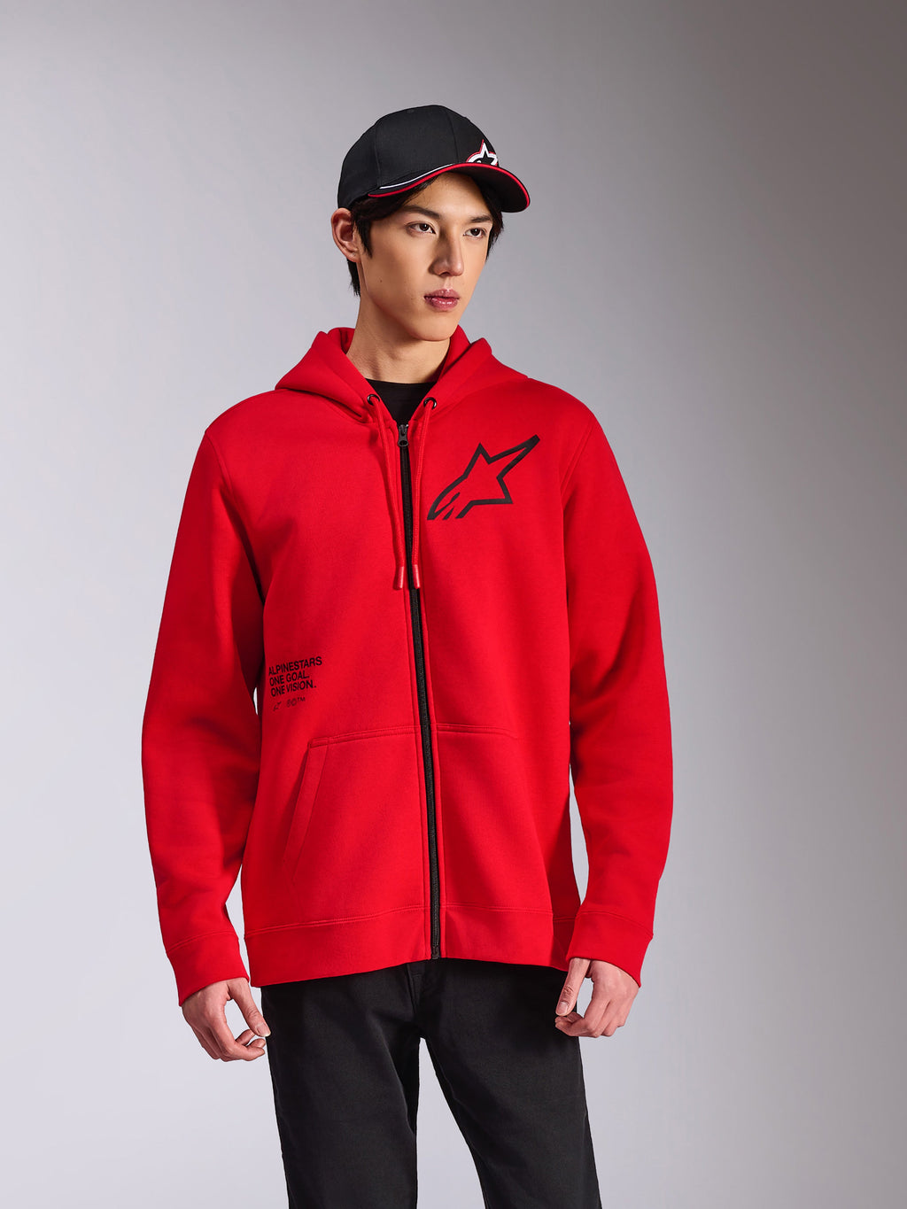 Alpinestars Transverse Hoodie, camisola vermelha com capuz e fecho frontal em tecido polar, logótipo Astars preto no peito e impressão 'One Goal', estilo casual streetwear usado com boné e calças pretas
