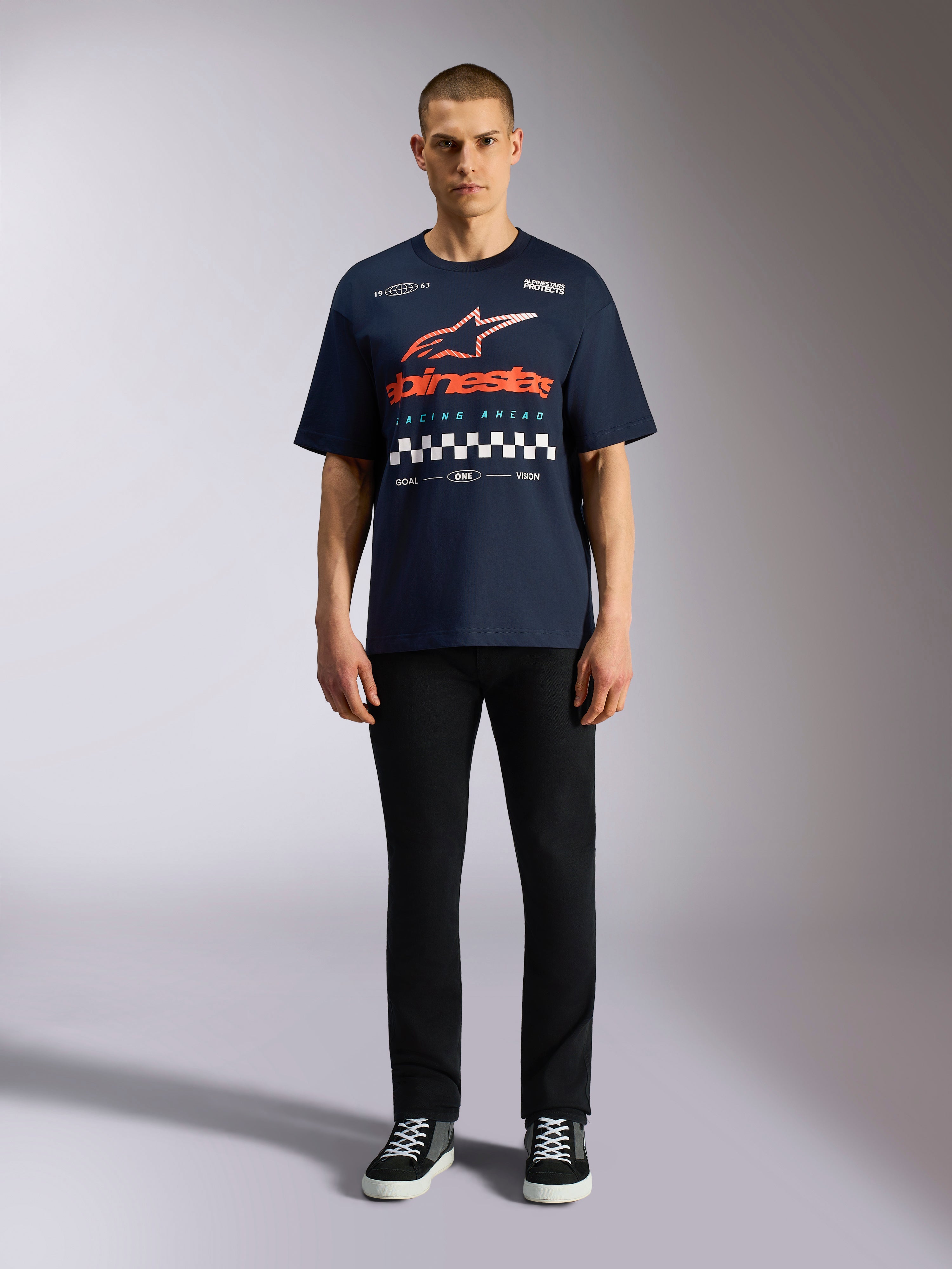 T-shirt Alpinestars Aplomb Oversized CSF, t-shirt de manga curta azul marinho, logótipo grande no peito com gradiente laranja e vermelho e padrão axadrezado, usada por modelo com calças pretas e sapatilhas, streetwear casual de inspiração motorsport