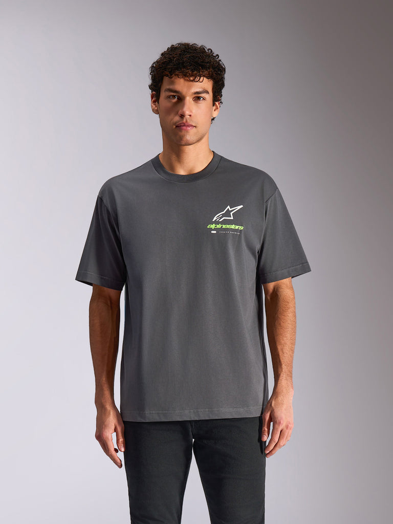 Alpinestars Overhang Oversized CSF Tee, t-shirt de manga curta em cinza carvão, logótipo Astars branco e marca em verde lima no peito, corte oversized, modelo masculino a vestir a t-shirt com calças pretas, estilo streetwear casual de inspiração motorizada
