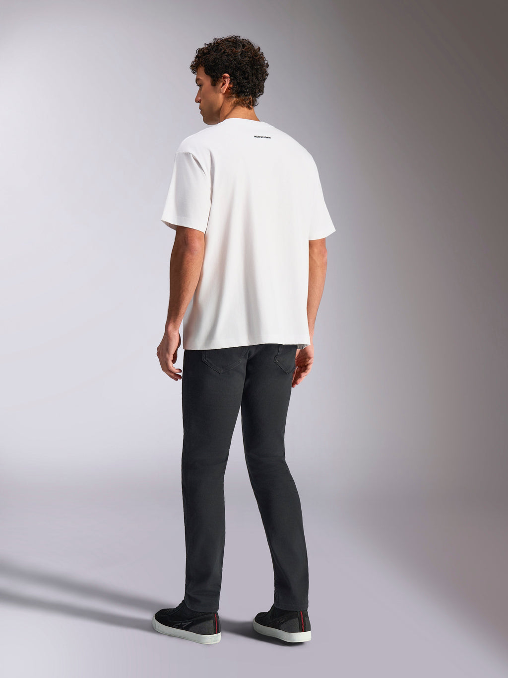 T-shirt Alpinestars Focused Oversized CSF, t-shirt de manga curta, branca, pequeno logótipo da palavra Alpinestars a preto na parte de trás da gola, usada com calças pretas, corte oversized, streetwear casual inspirado no desporto motorizado