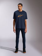 T-shirt Alpinestars Alter Oversized CSF, t-shirt de manga curta, azul-marinho, com o logótipo frontal da estrela Alpinestars com desvio de cor em amarelo e laranja, usada por um modelo com calças de ganga escuras e ténis pretos, vestuário desportivo casual.