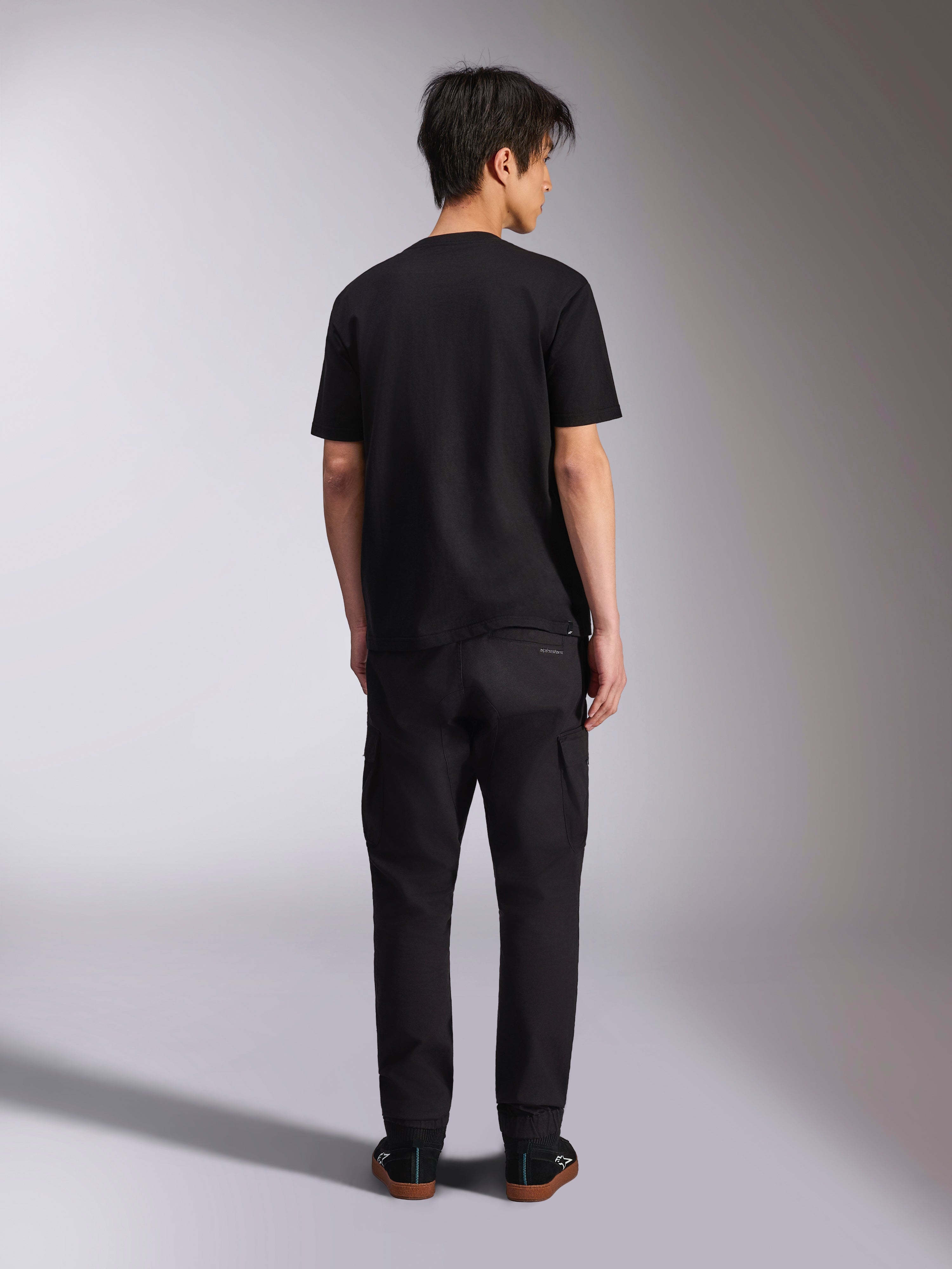 Alpinestars Noka CSF Tee, Short Sleeve T-Shirt, Black, back view of model wearing the tee with black pants and sneakers, casual motorsport streetwear style
